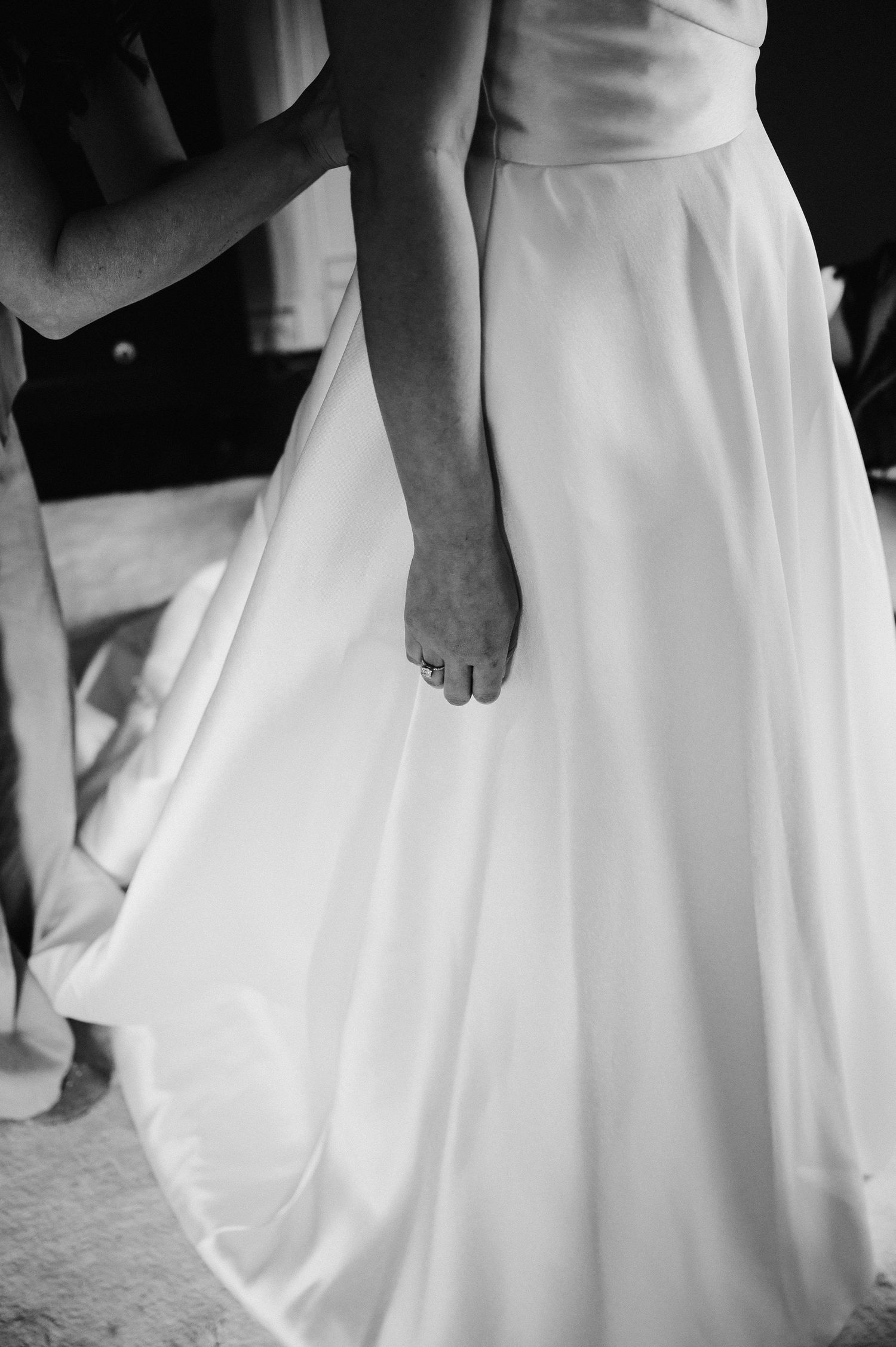 Black and white photo of a bride in a flowing white wedding gown with an engagement ring visible on her hand.