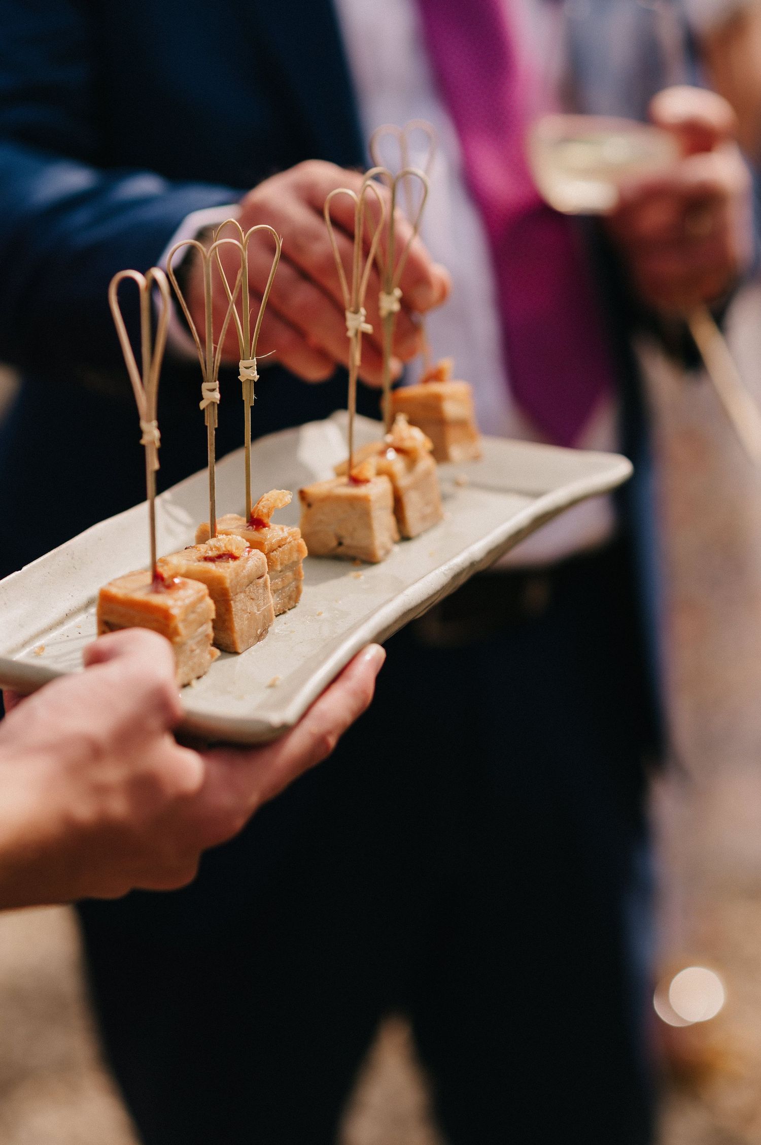 Elegant appetizer skewers on a ceramic tray held by a server at a catered event.