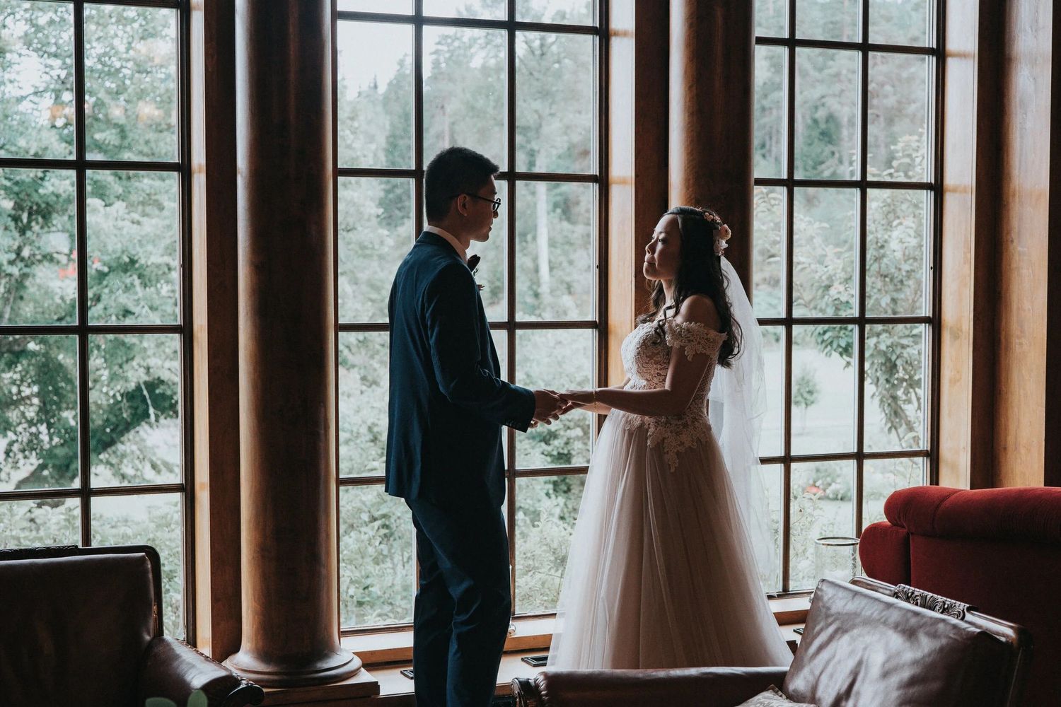 Silhouetted couple poses by large windows in rustic venue.