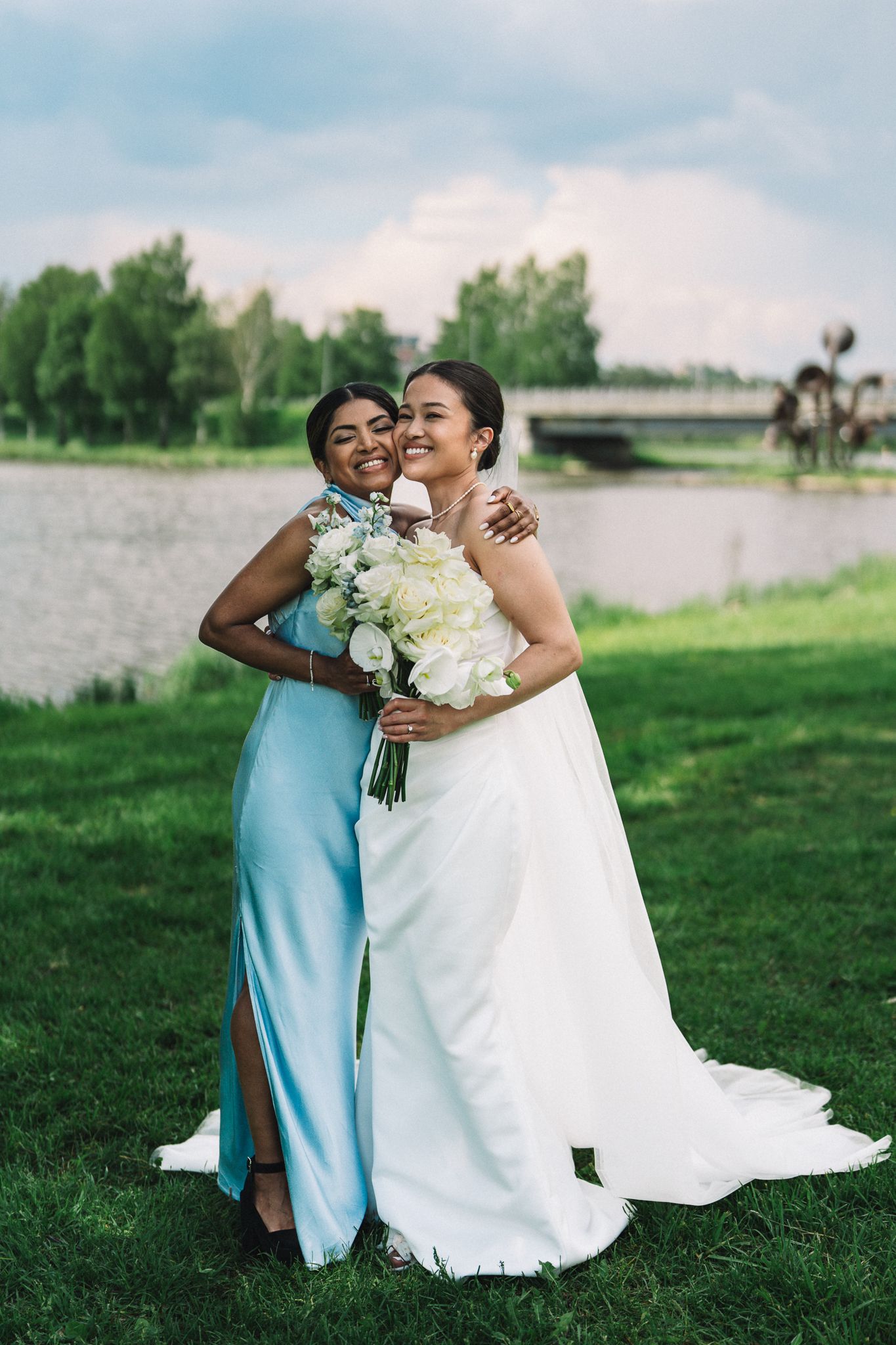 Wedding couple embracing on green grass with white bouquet and light blue bridesmaid dress.