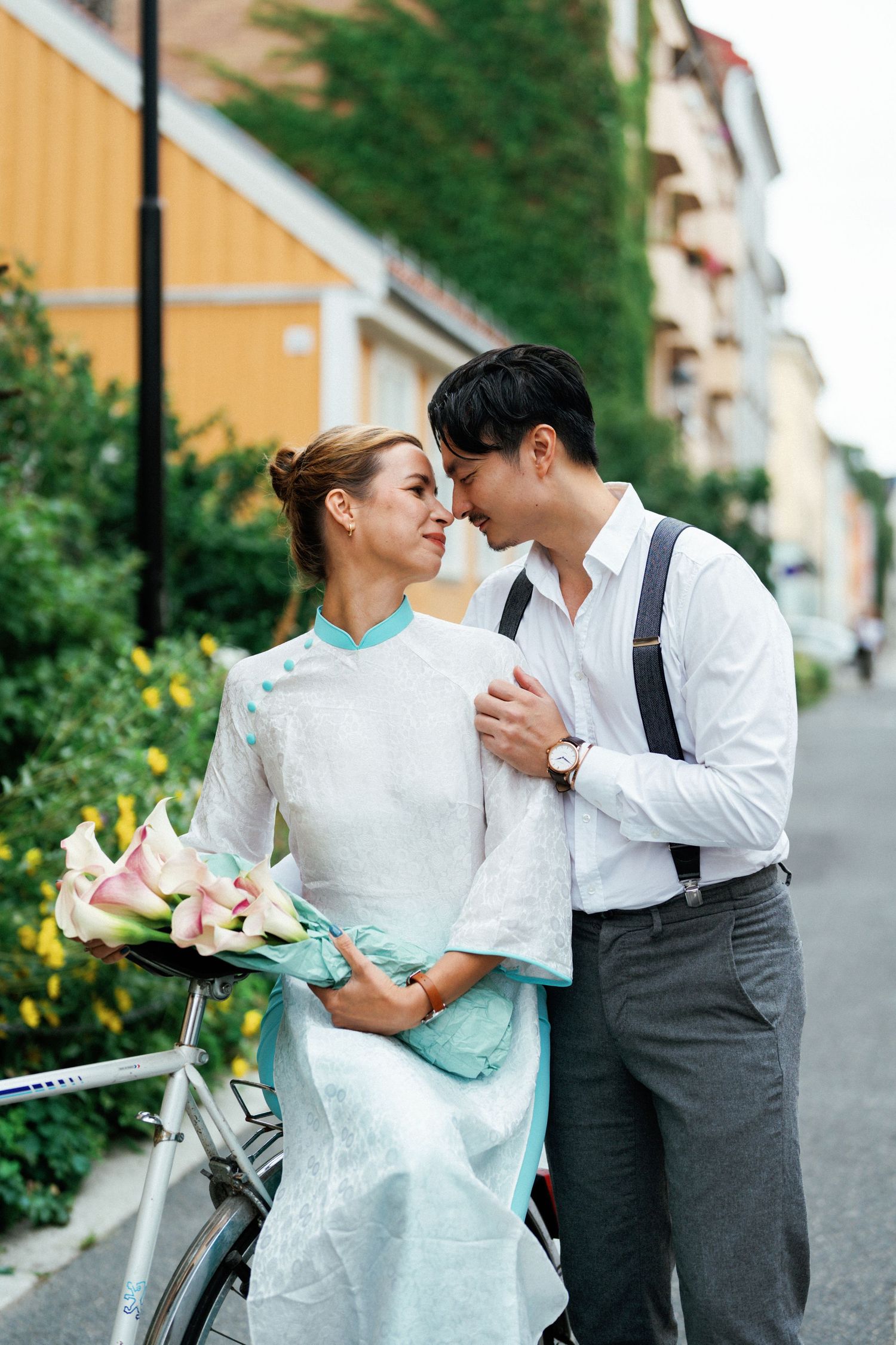 A romantic couple in vintage-inspired attire share tender moments beside a bicycle on a charming European street.