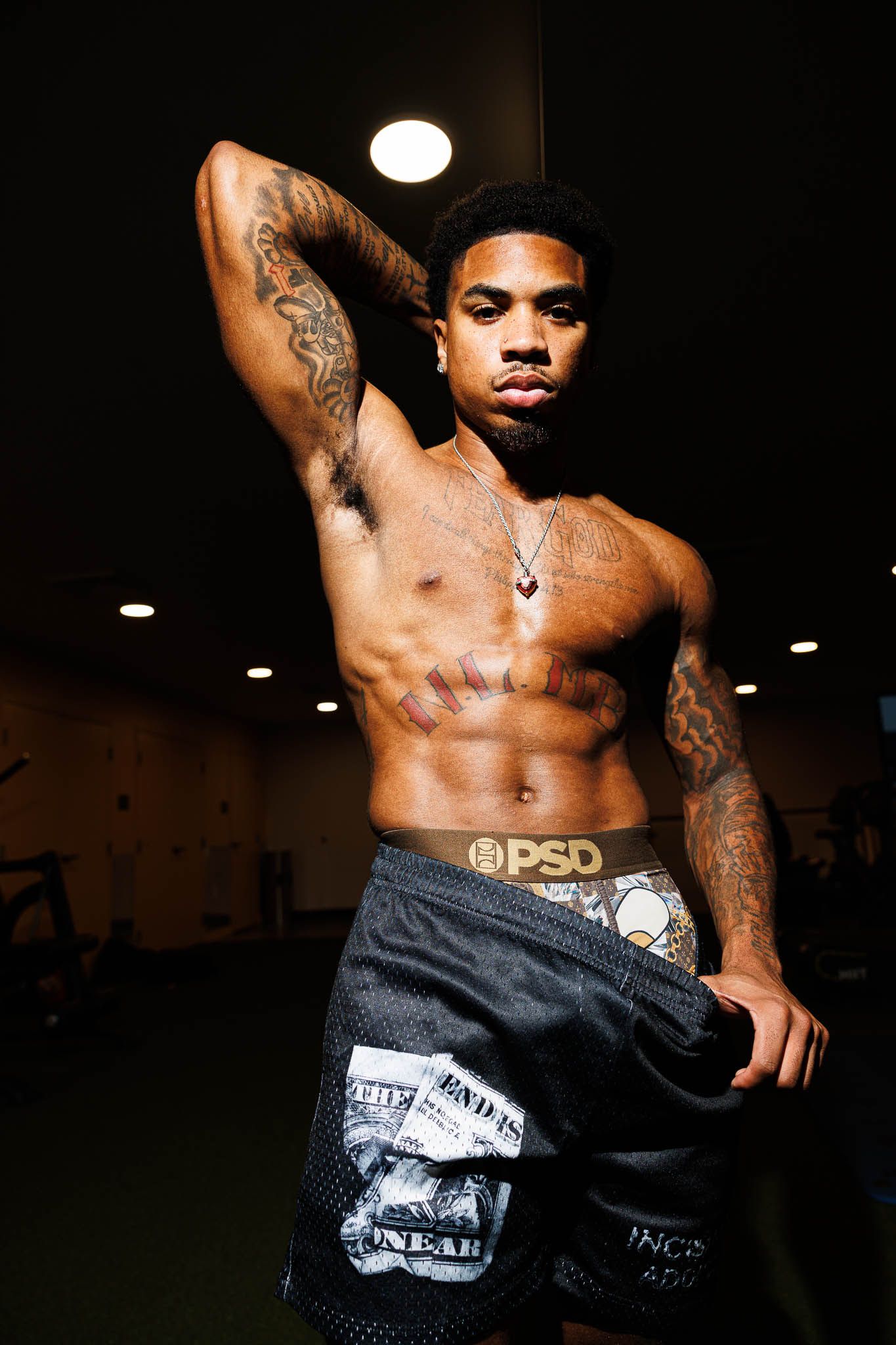 Athletic figure showing off tattoos and muscles in dramatic lighting while wearing PSD shorts.