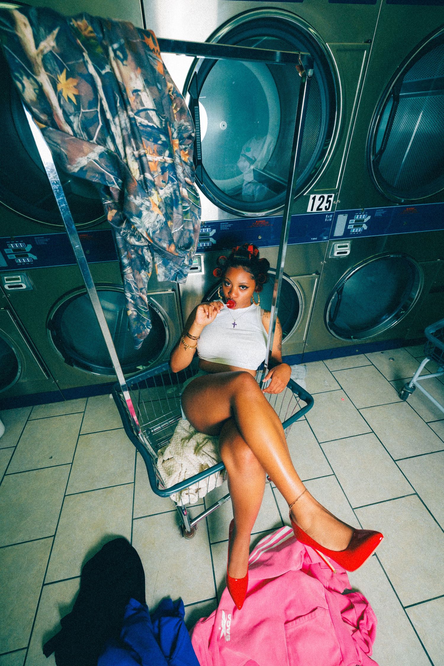 Woman in white top and red heels relaxing in a laundry cart at a colorful laundromat.