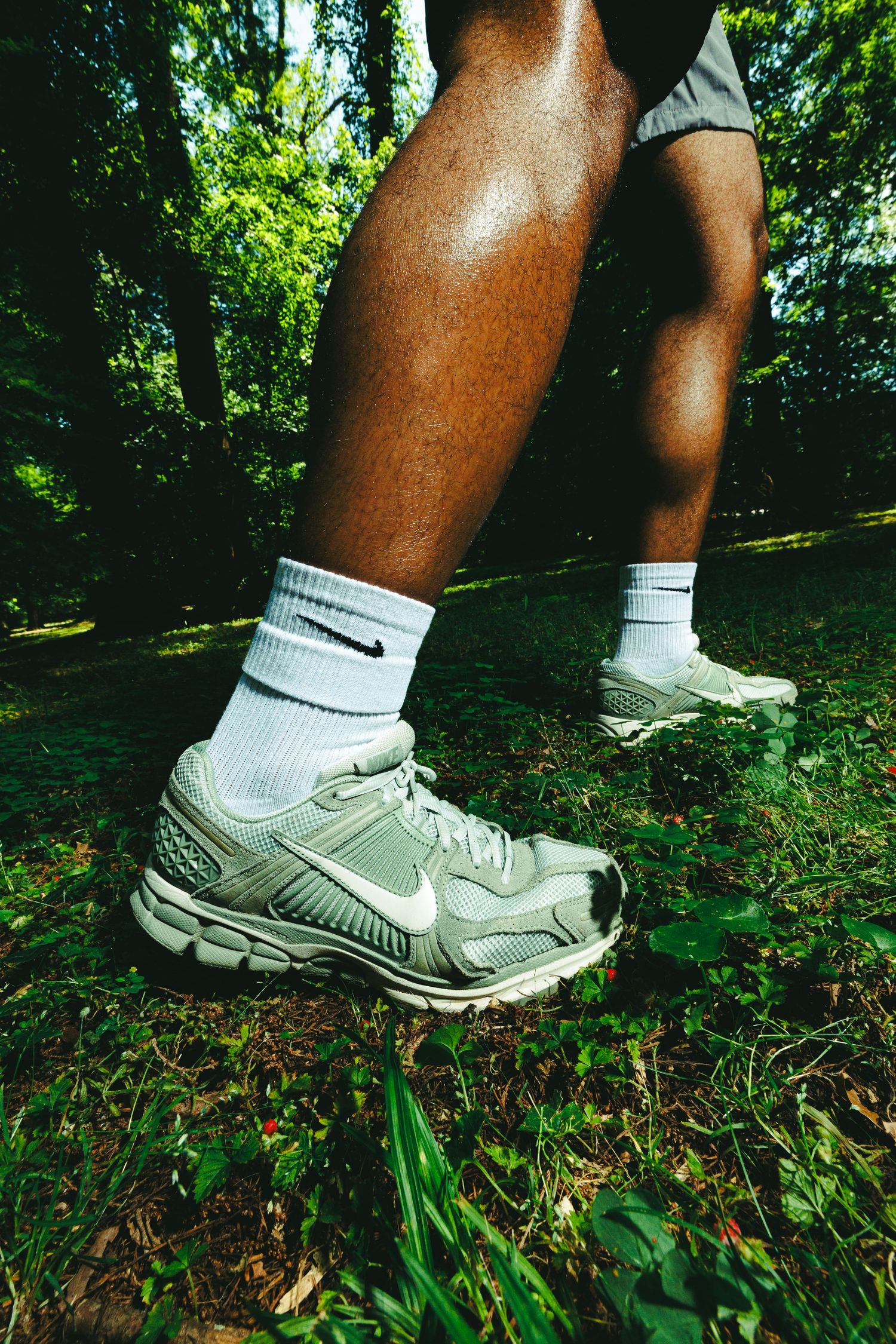 Close-up of Nike Zoom Vomero sneakers in sage green with white socks on a person running through a forest.