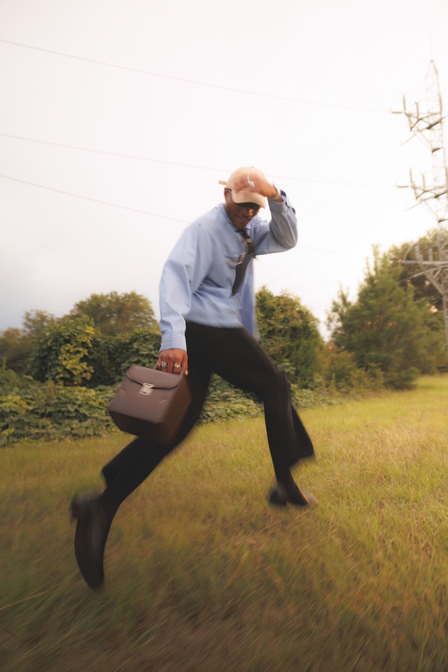 Editorial commercial photograph of a businessman running through an open field with a briefcase, capturing movement, ambition, and cinematic