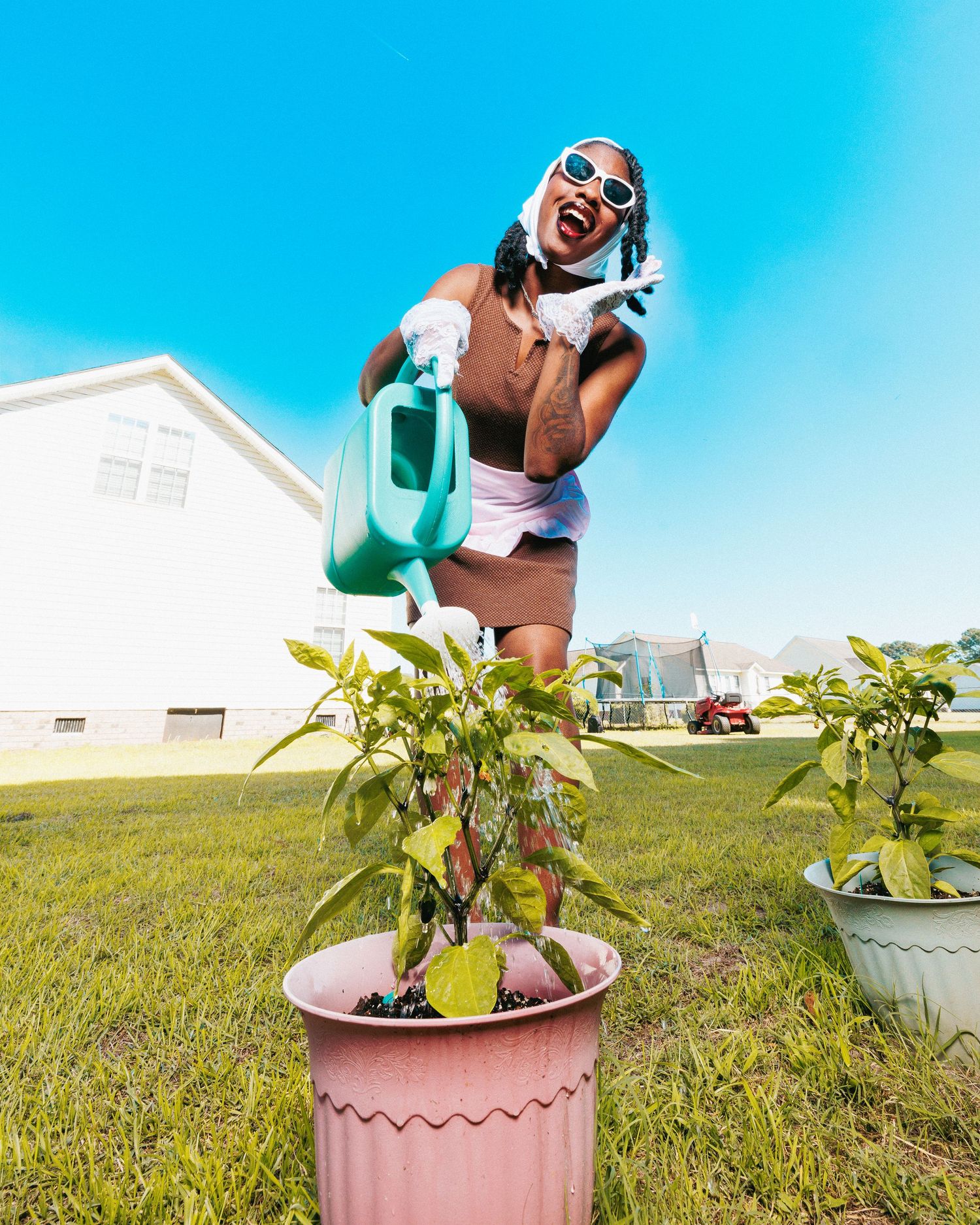 A joyful woman in sunglasses watering a potted plant outdoors on a sunny day.