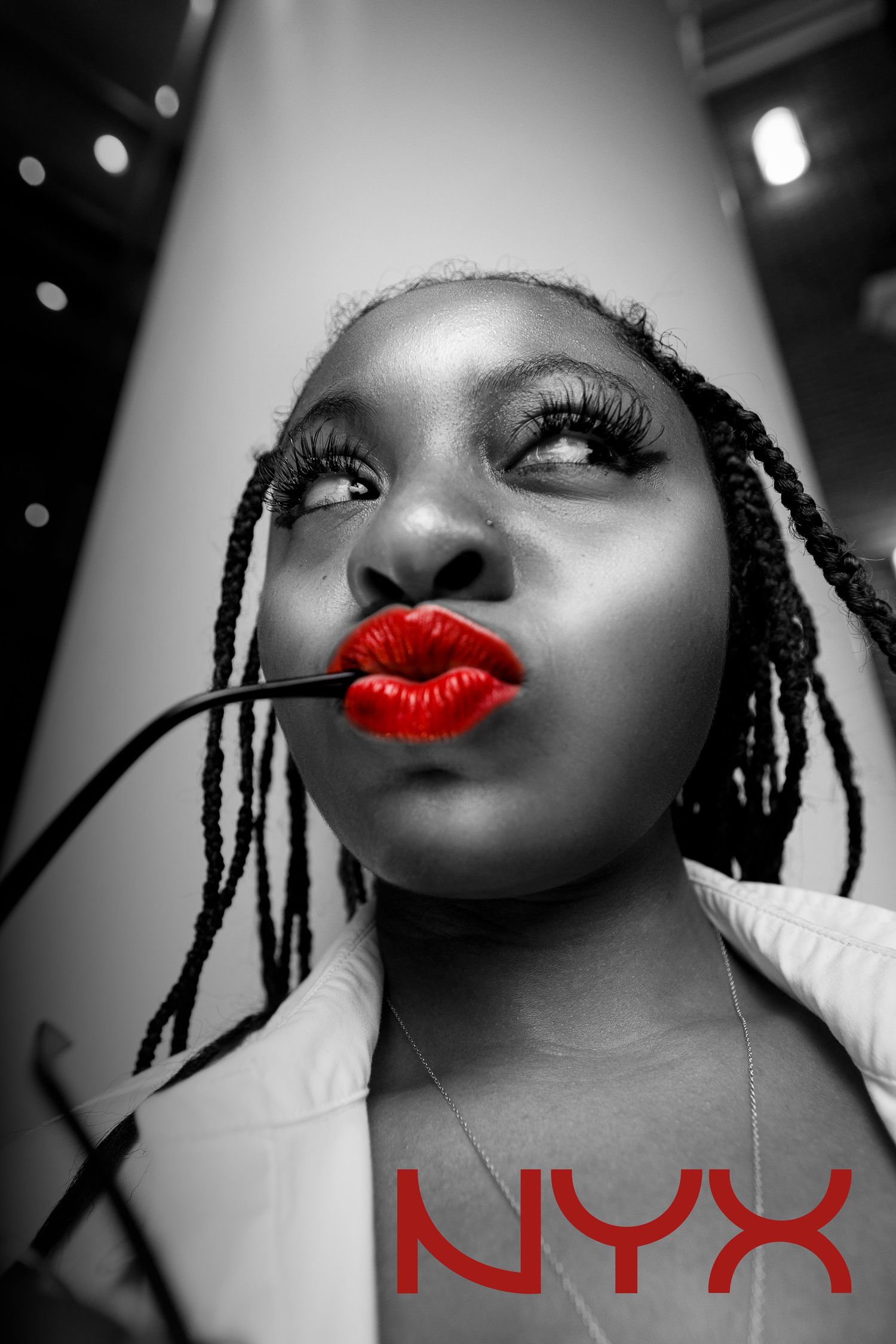 Black and white portrait of a woman with braids and bold red lips holding a NYX lip liner brush.