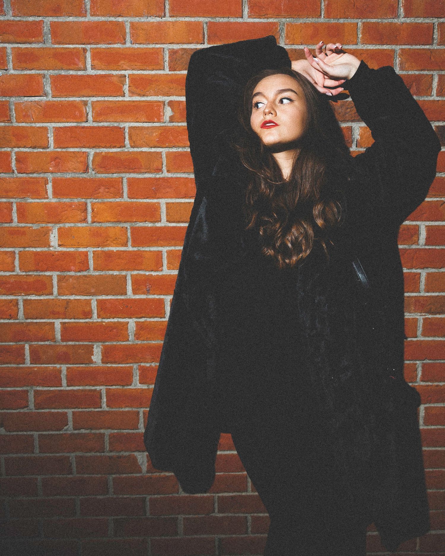 Figure in dark clothing against brick wall with dramatic lighting.