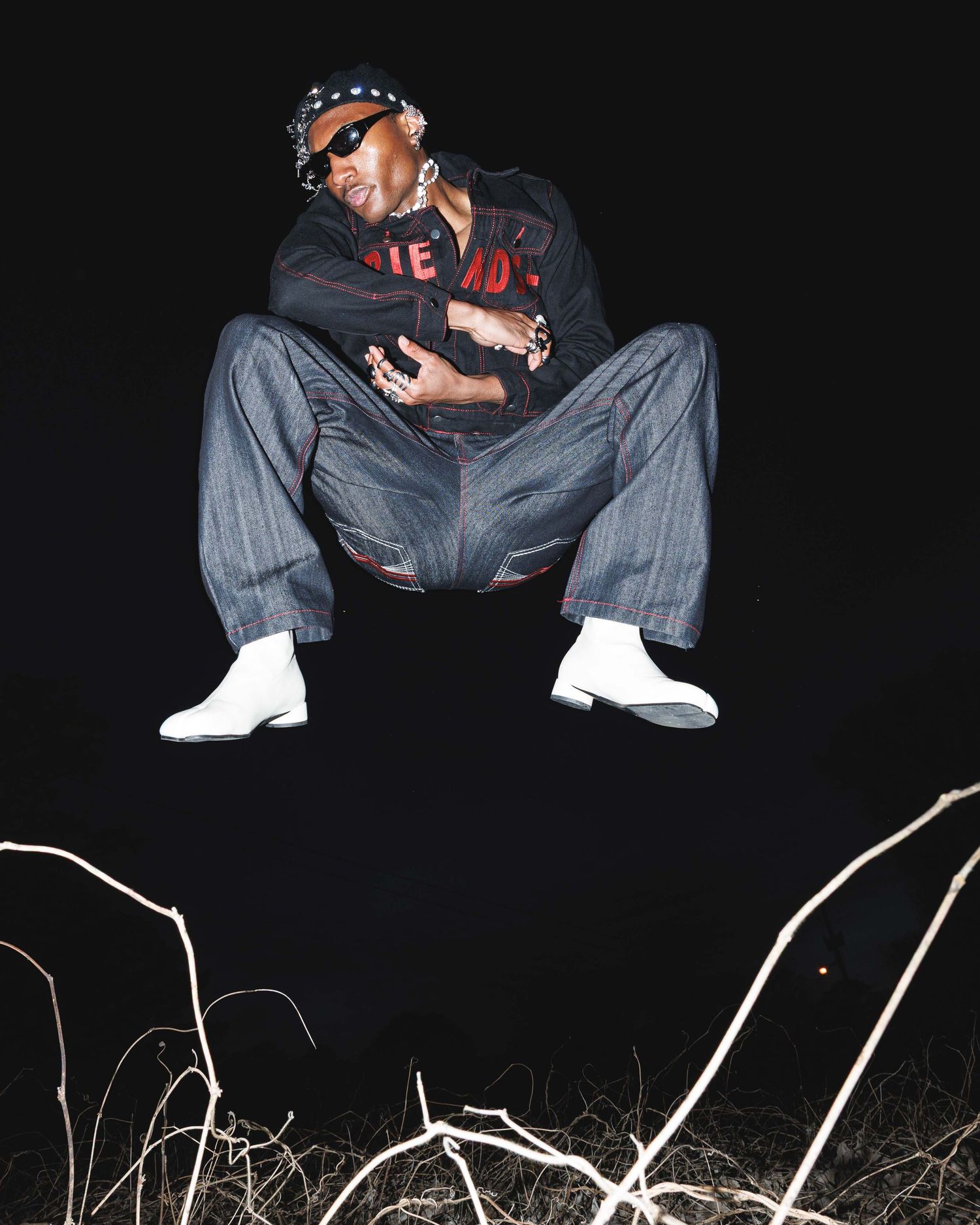 Person in dark clothing sitting on ground against black background with white lines.