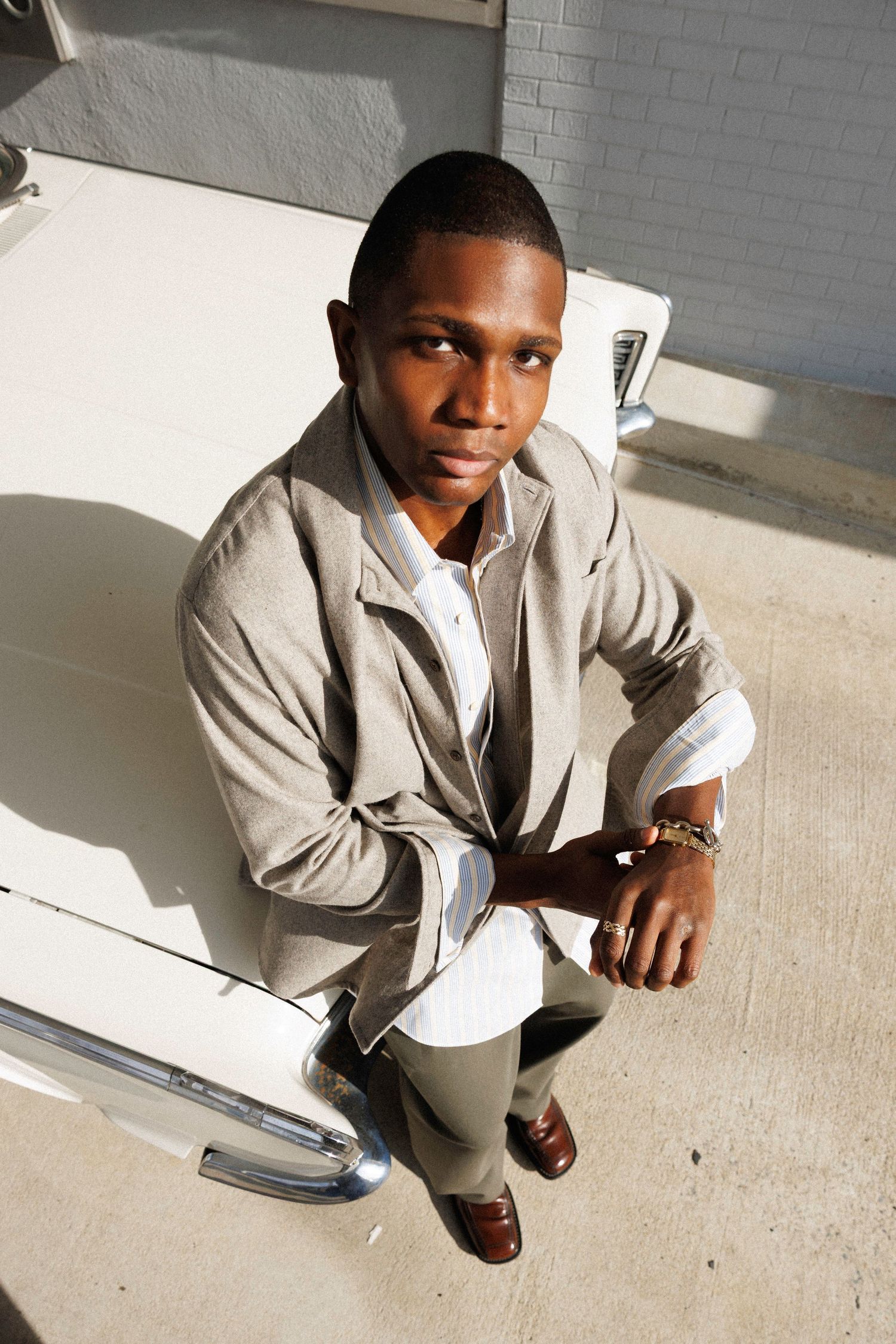 Fashion portrait series showing model in beige suit against white wall with dramatic lighting.
