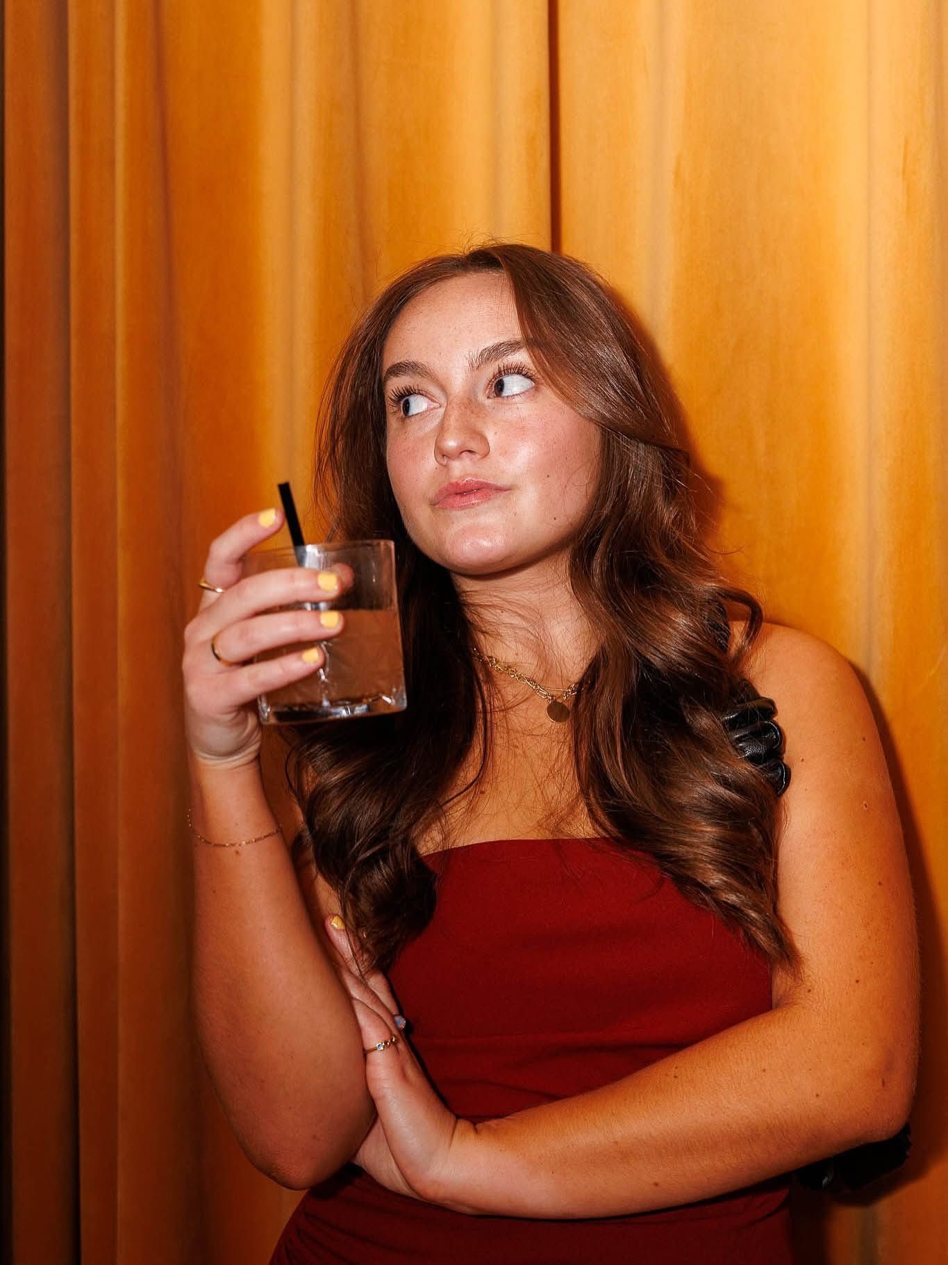 Person in burgundy top with drink against orange backdrop in sequential portraits.