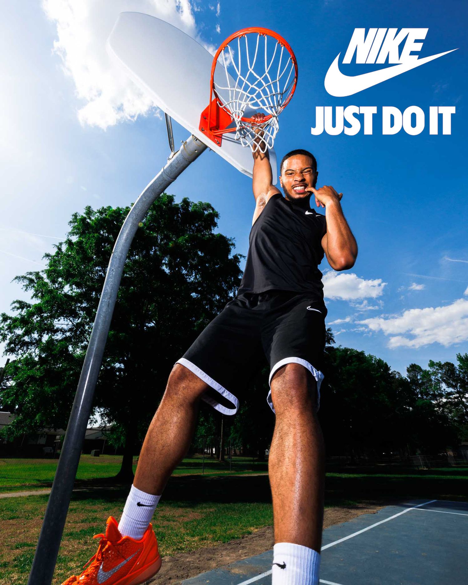 Man dunking basketball on outdoor court wearing Nike gear, with Just Do It logo visible against blue sky.