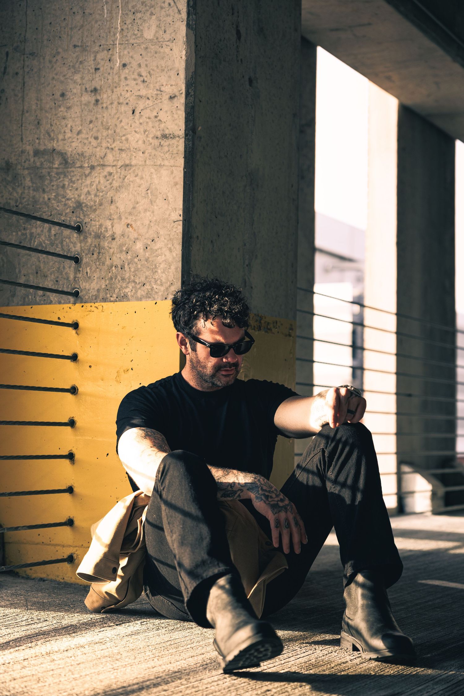 Artistic sequence showing person in black reclining against concrete pillar with yellow accent wall.