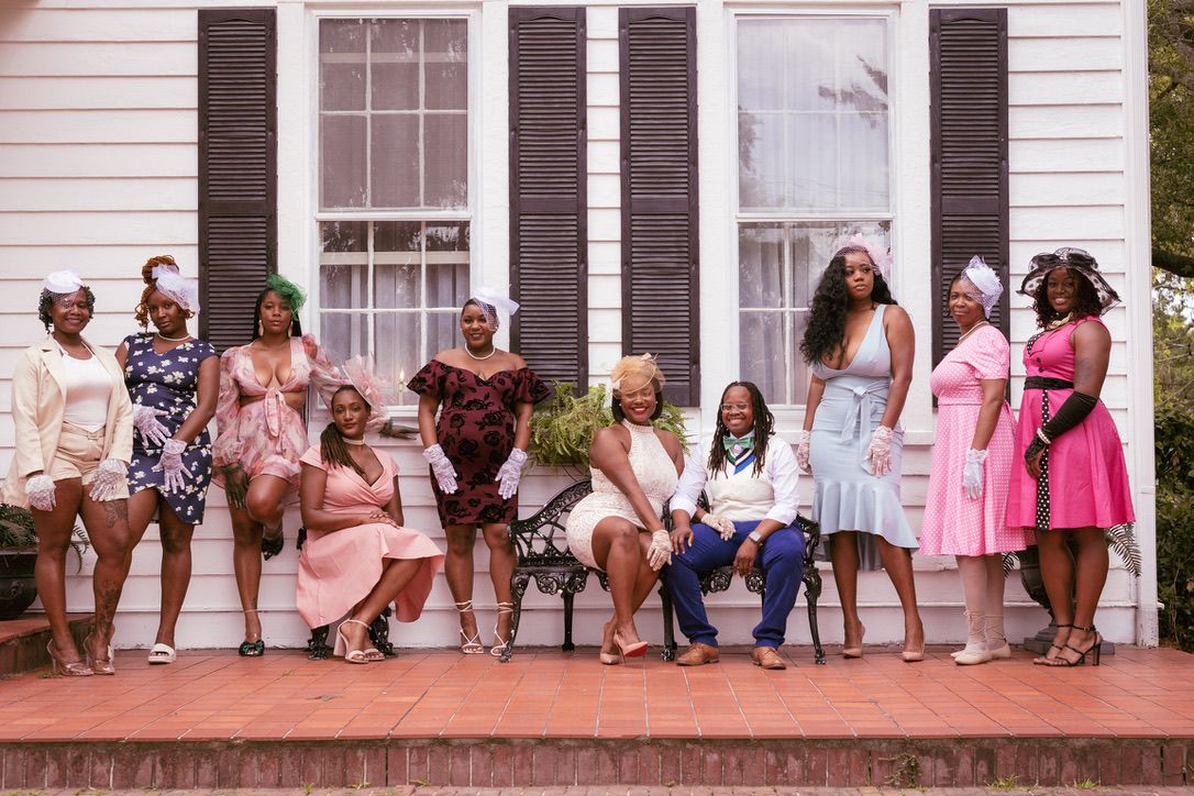 Group posing on front porch steps of a white house with black shutters.