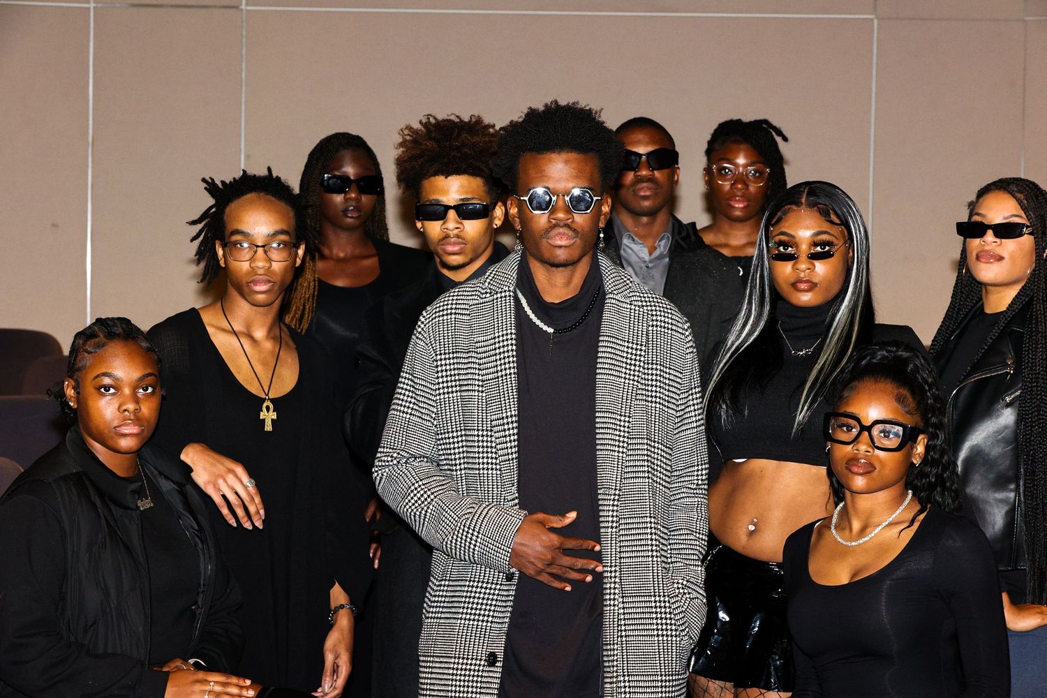 Group photo of stylishly dressed people in black and gray outfits against white background.