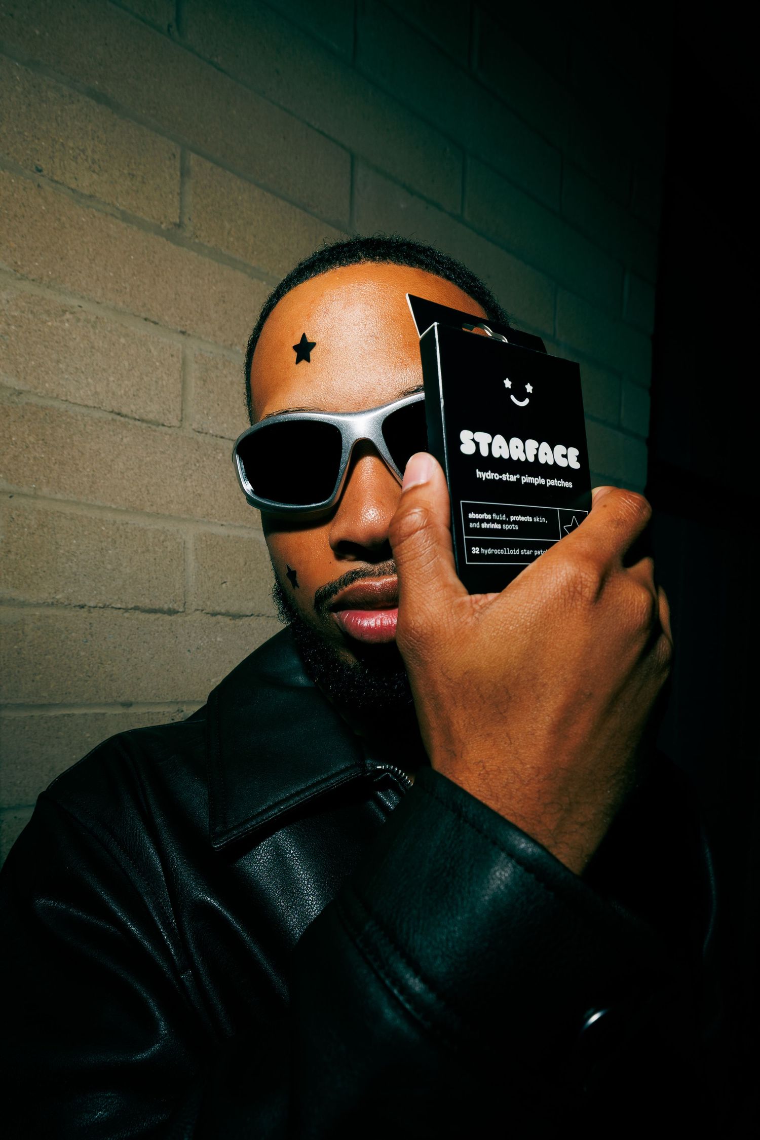 Man wearing sunglasses and a star face patch holds a Starface hydro-star pimple patch box.