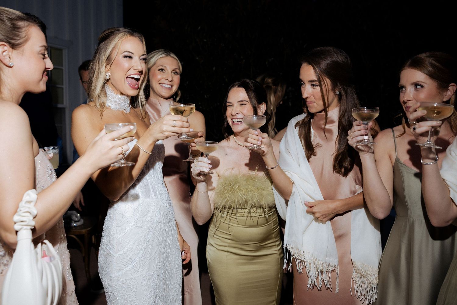 A group of wedding guests in formal attire laugh and smile together during a celebratory moment at a reception.