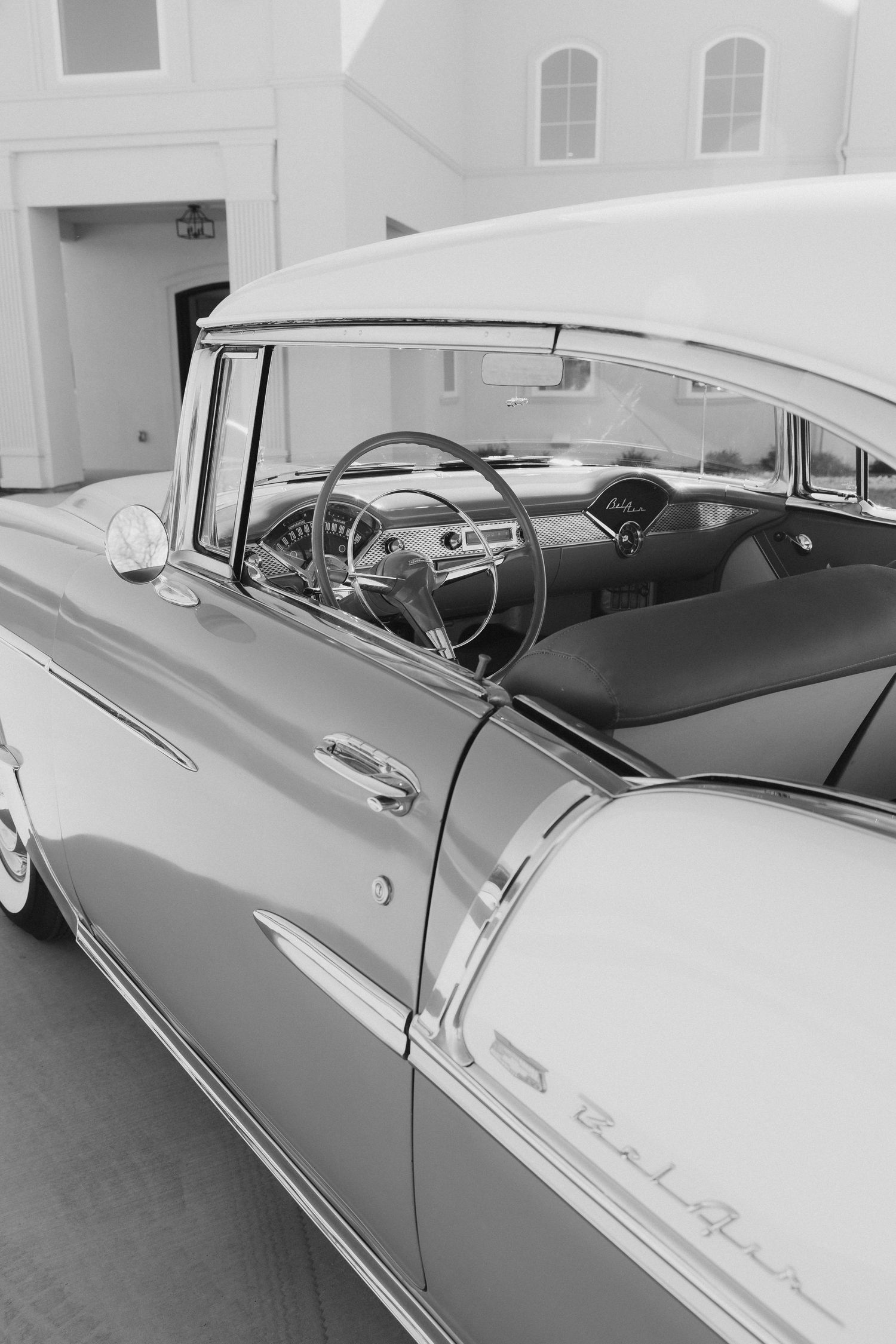 Close-up view of a classic 1950s Chevrolet Bel Air car interior and side panel showing vintage steering wheel and chrome details.