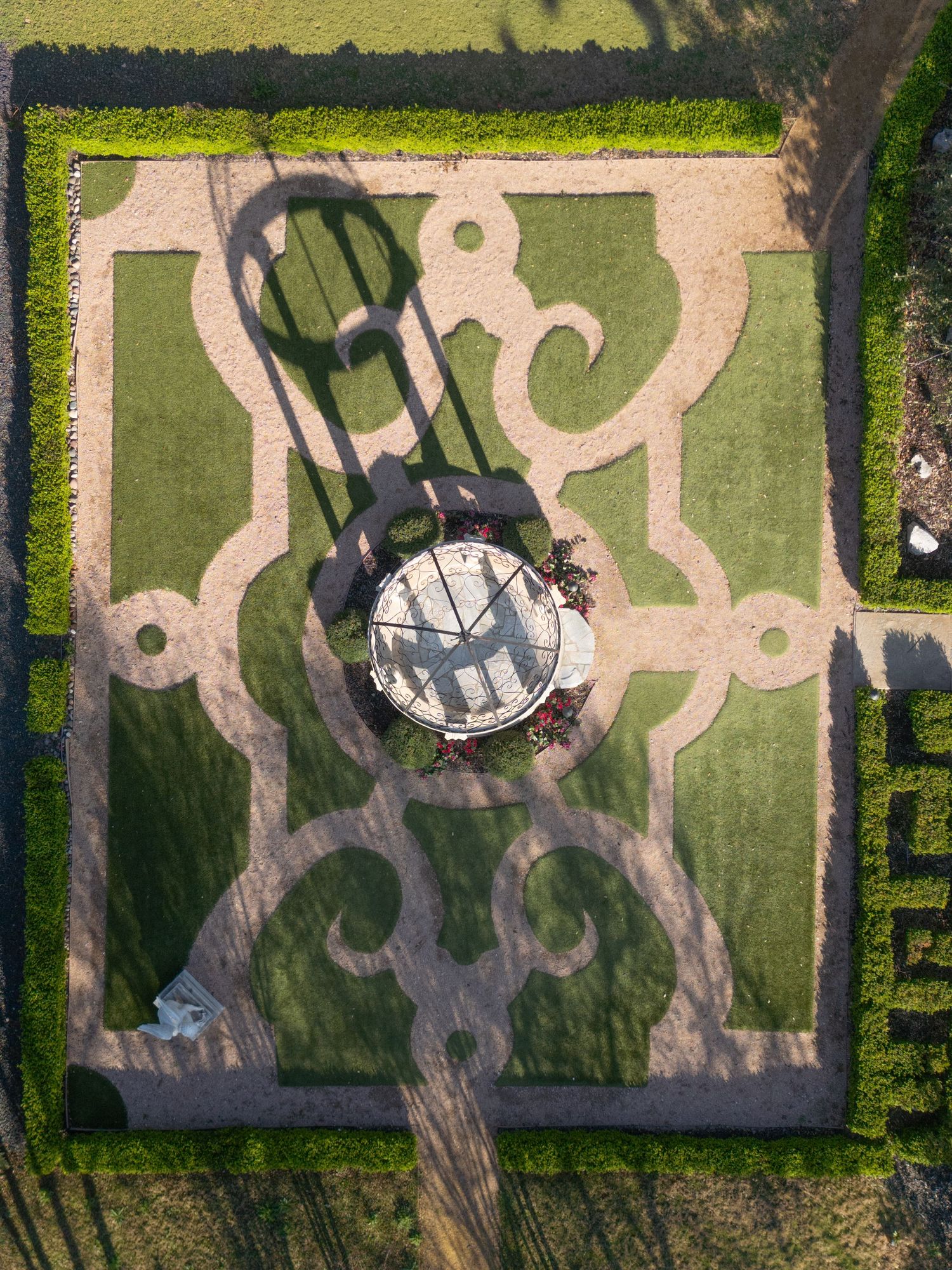 Aerial view of a formal garden with ornate green hedgerow patterns surrounding a circular sundial centerpiece.