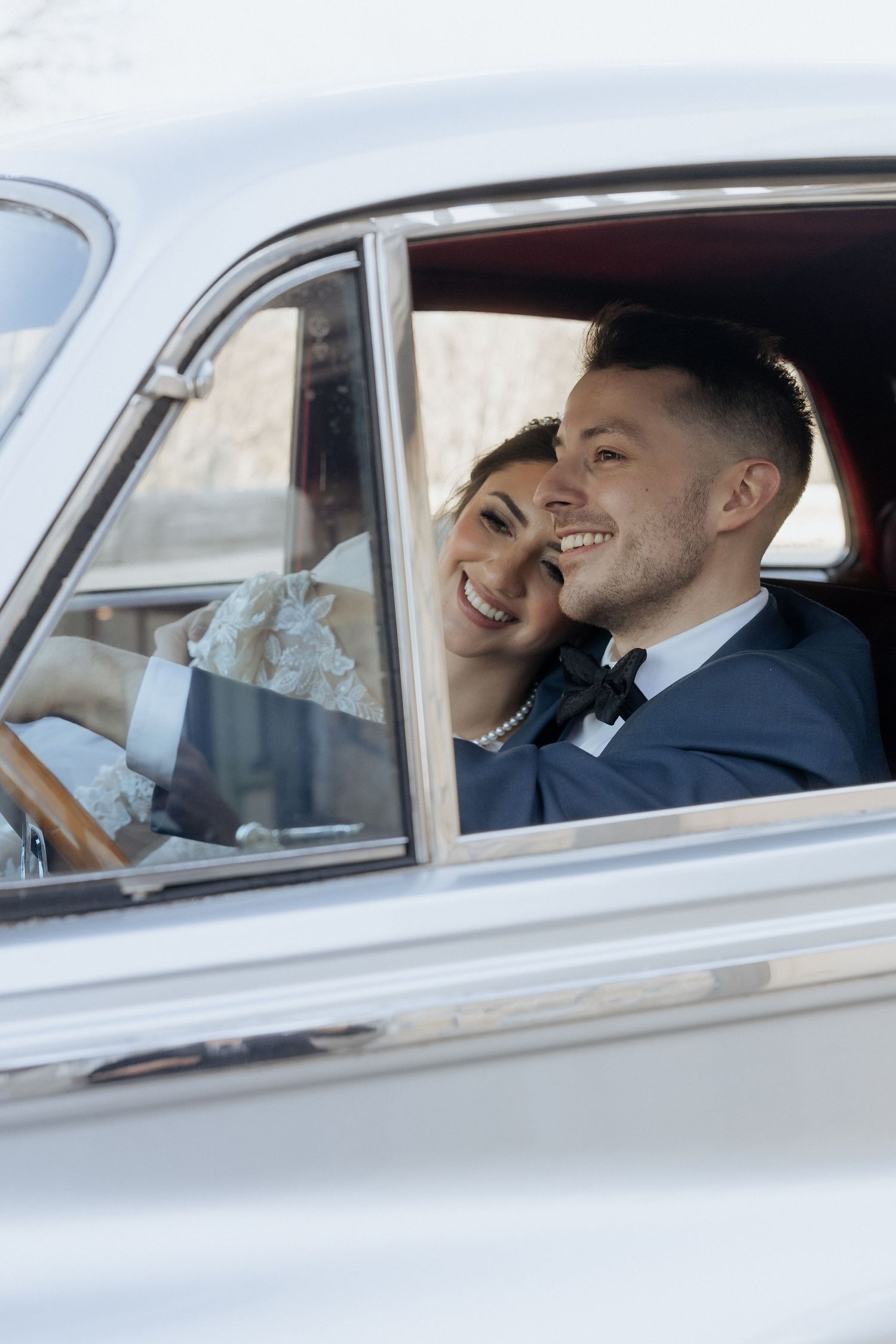 Newlywed couple sharing a joyful moment together in a classic car after their wedding ceremony.
