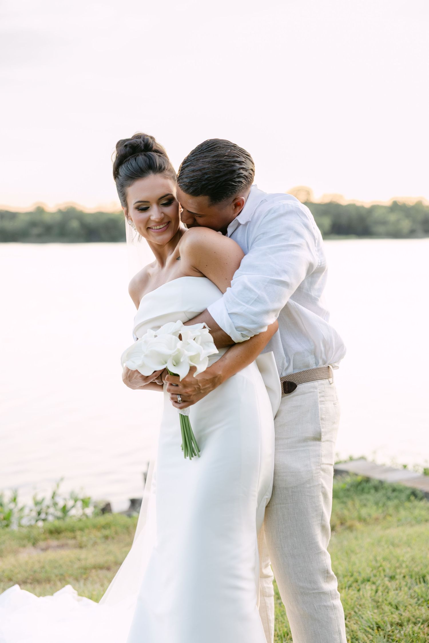 A romantic couple in white attire shares tender moments during their seaside wedding photoshoot.