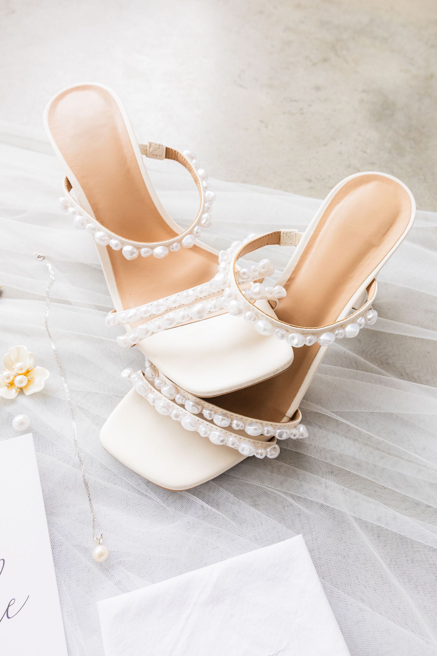 Elegant white bridal sandals with pearl detailing on straps against light grey background.
