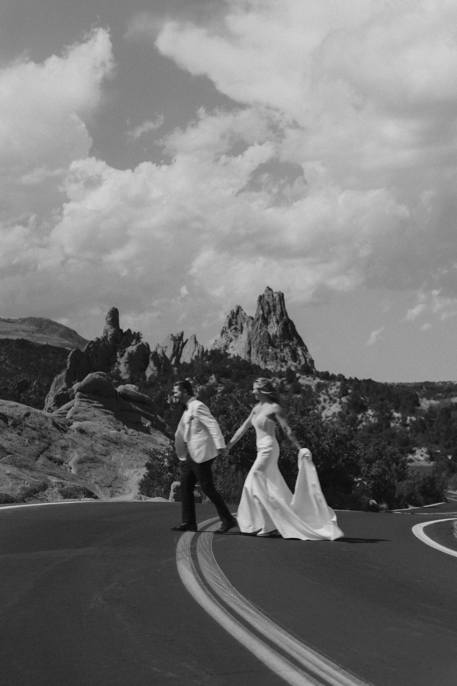 Black and white photo of a bride and groom holding hands crossing a road at Garden of the Gods, Colorado.