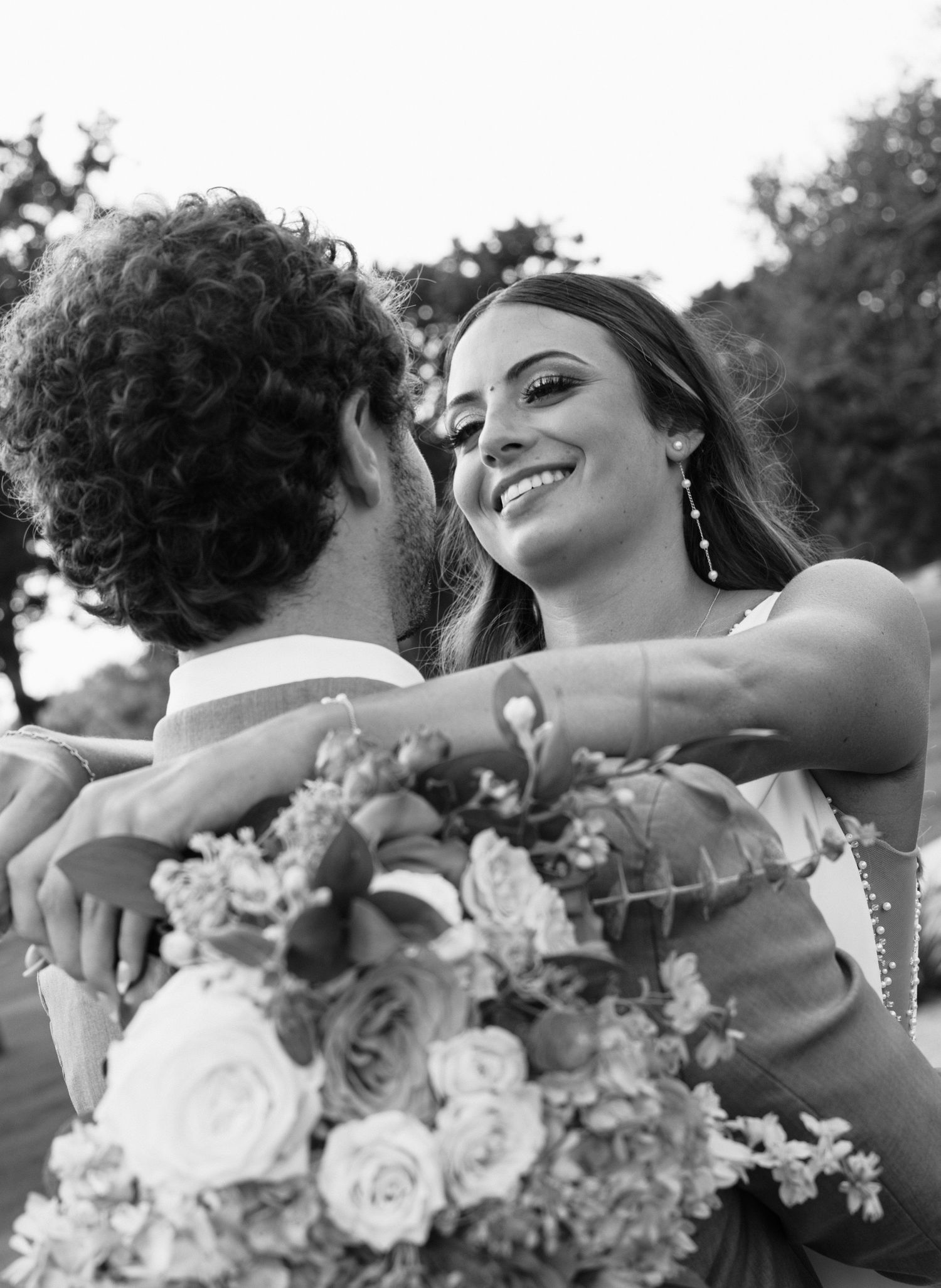 Black and white candid wedding photo showing a joyful moment with couple holding a beautiful floral bouquet of roses.