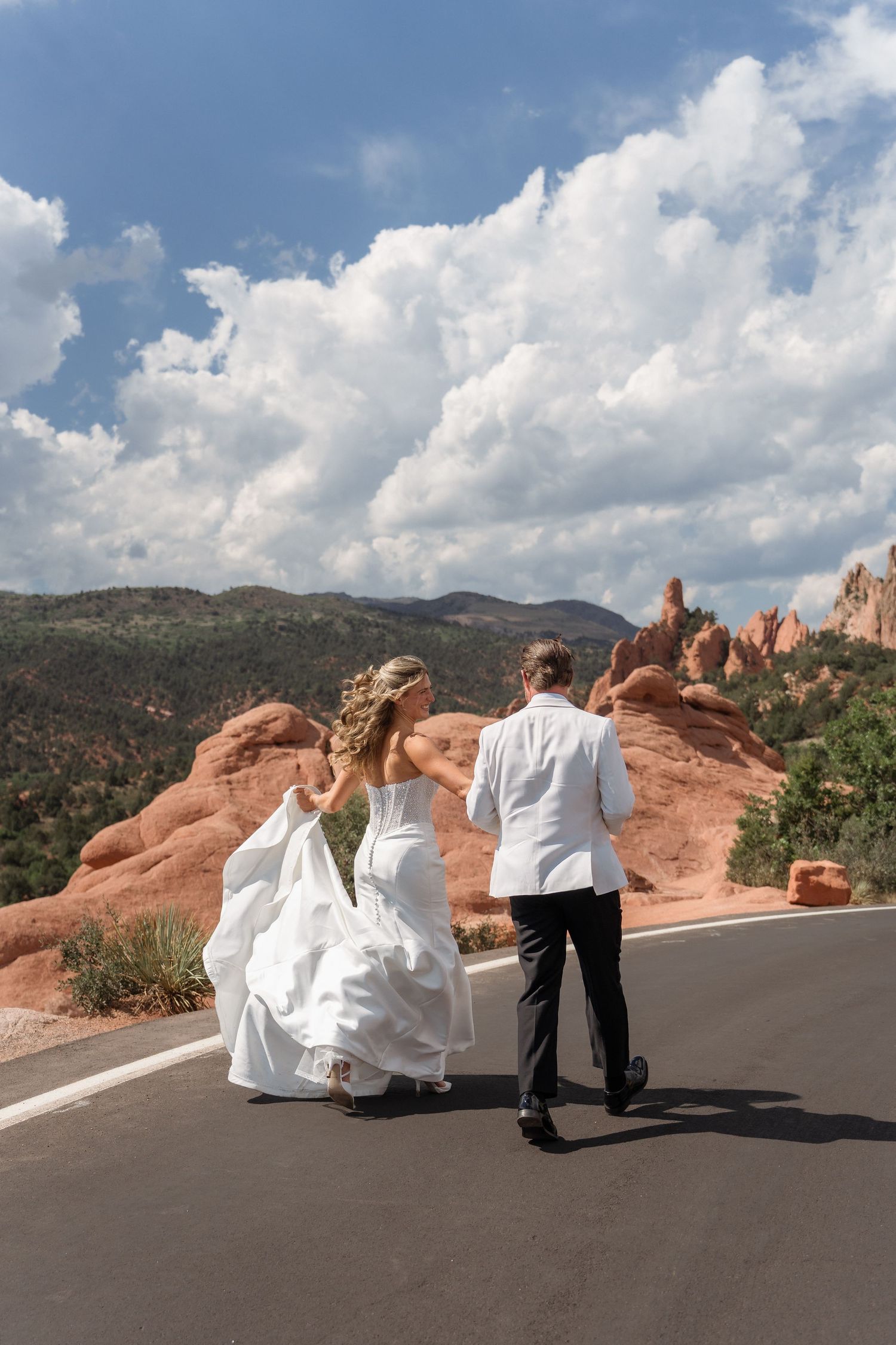 Bride and groom walking hand in hand on a road with red rock formations at Garden of the Gods, Colorado.
