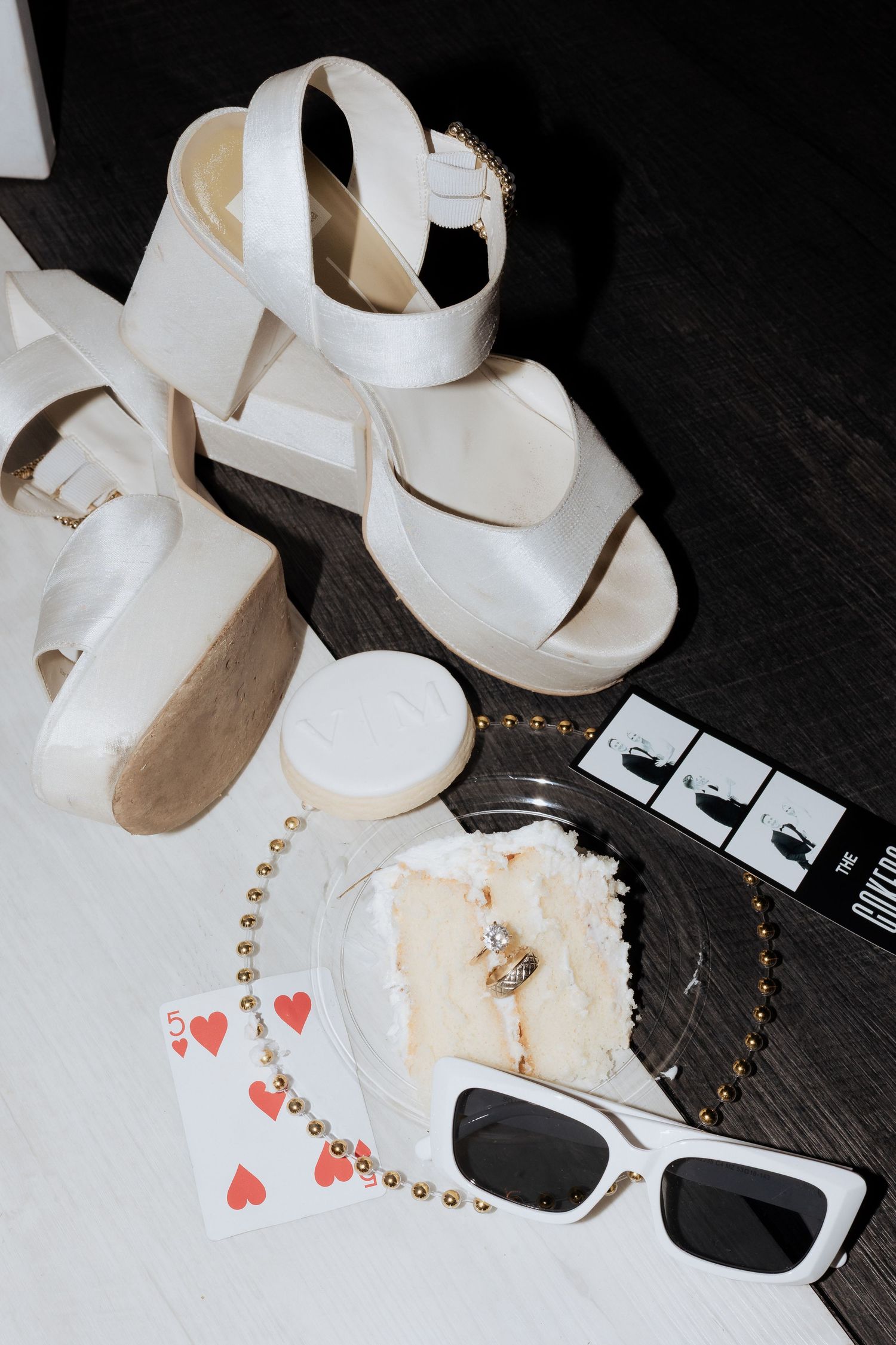 White ballet shoes and playing cards arranged artistically on a dark wooden surface with delicate silver beaded details.