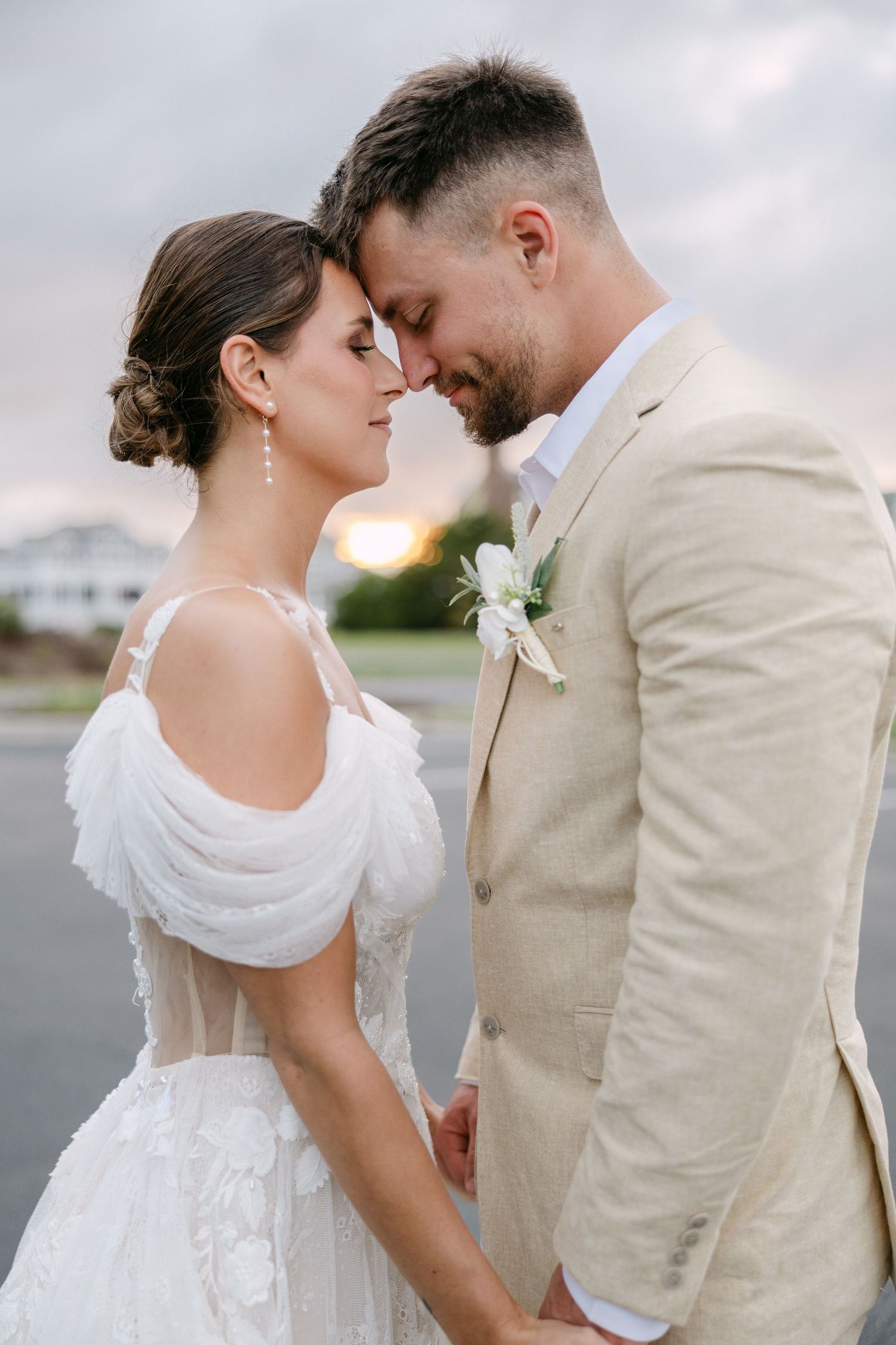 A romantic wedding couple shares an intimate moment at sunset, the bride in white and groom in beige.