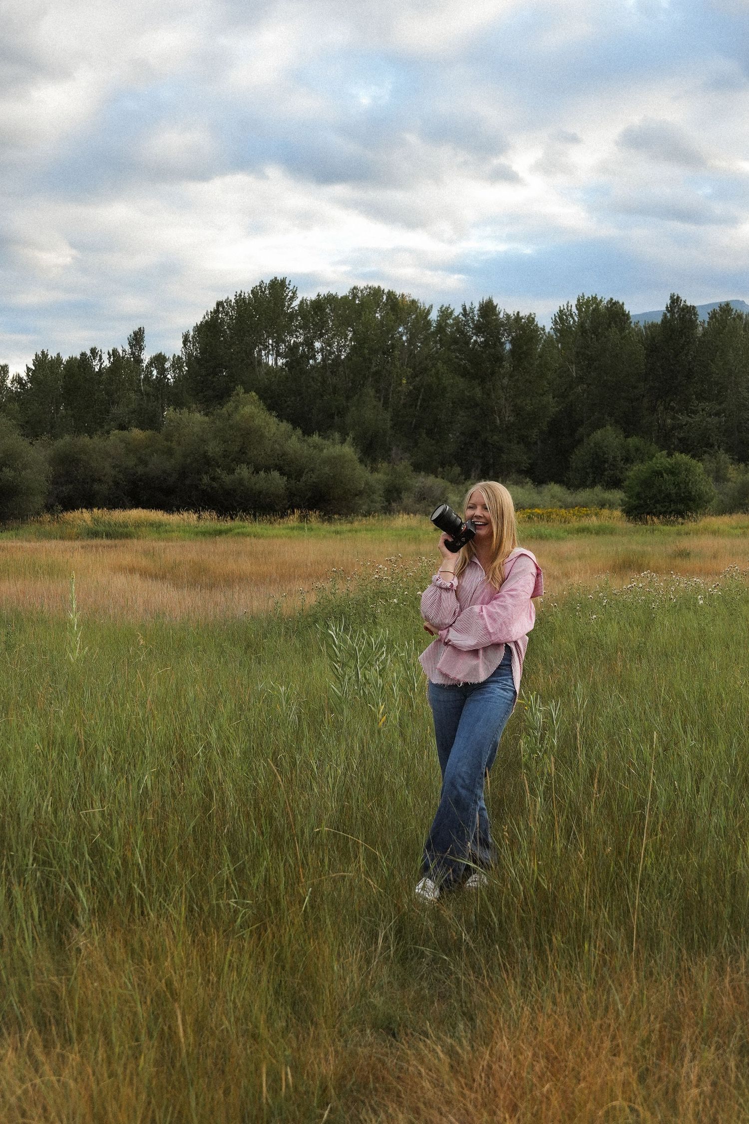 A photographer takes pictures in a tall grass field on an overcast day.