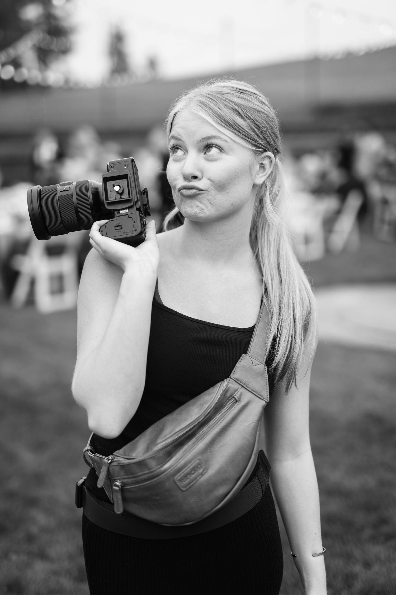 A photographer in a black tank top holds a telephoto lens camera while taking pictures outdoors.