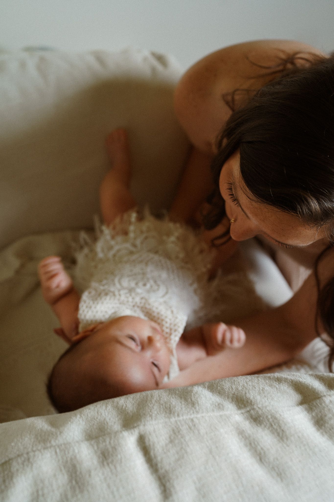 A sleeping infant wrapped in soft white blankets rests peacefully in natural lighting.