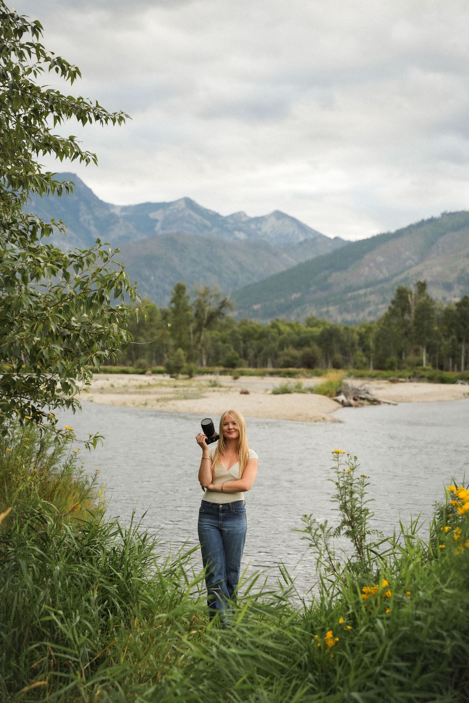 A scenic mountain landscape with a lake and wildflowers in the foreground during a cloudy summer day.