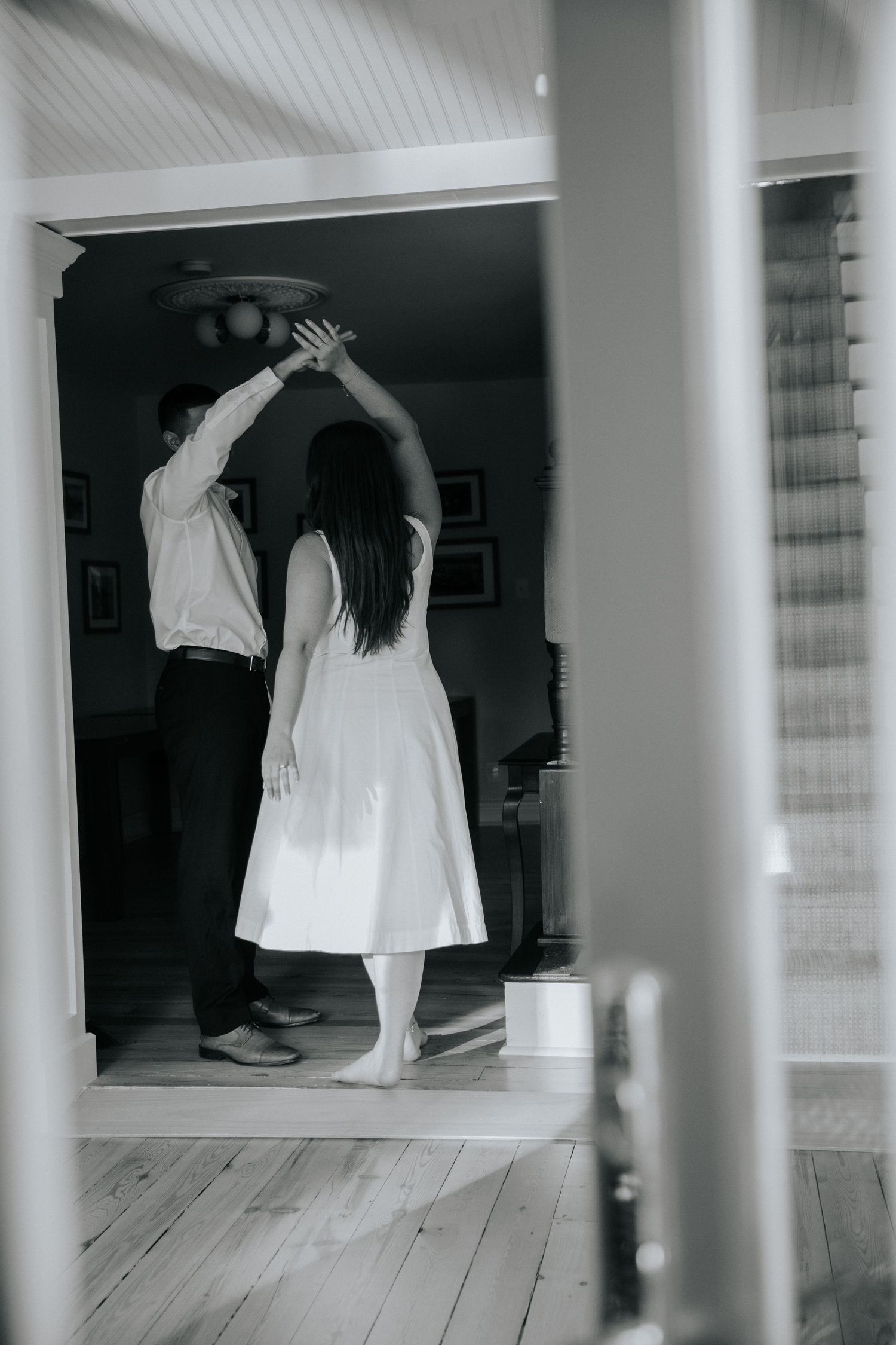 Multiple figures in white dresses move through a stark white room with columns creating an ethereal artistic scene.