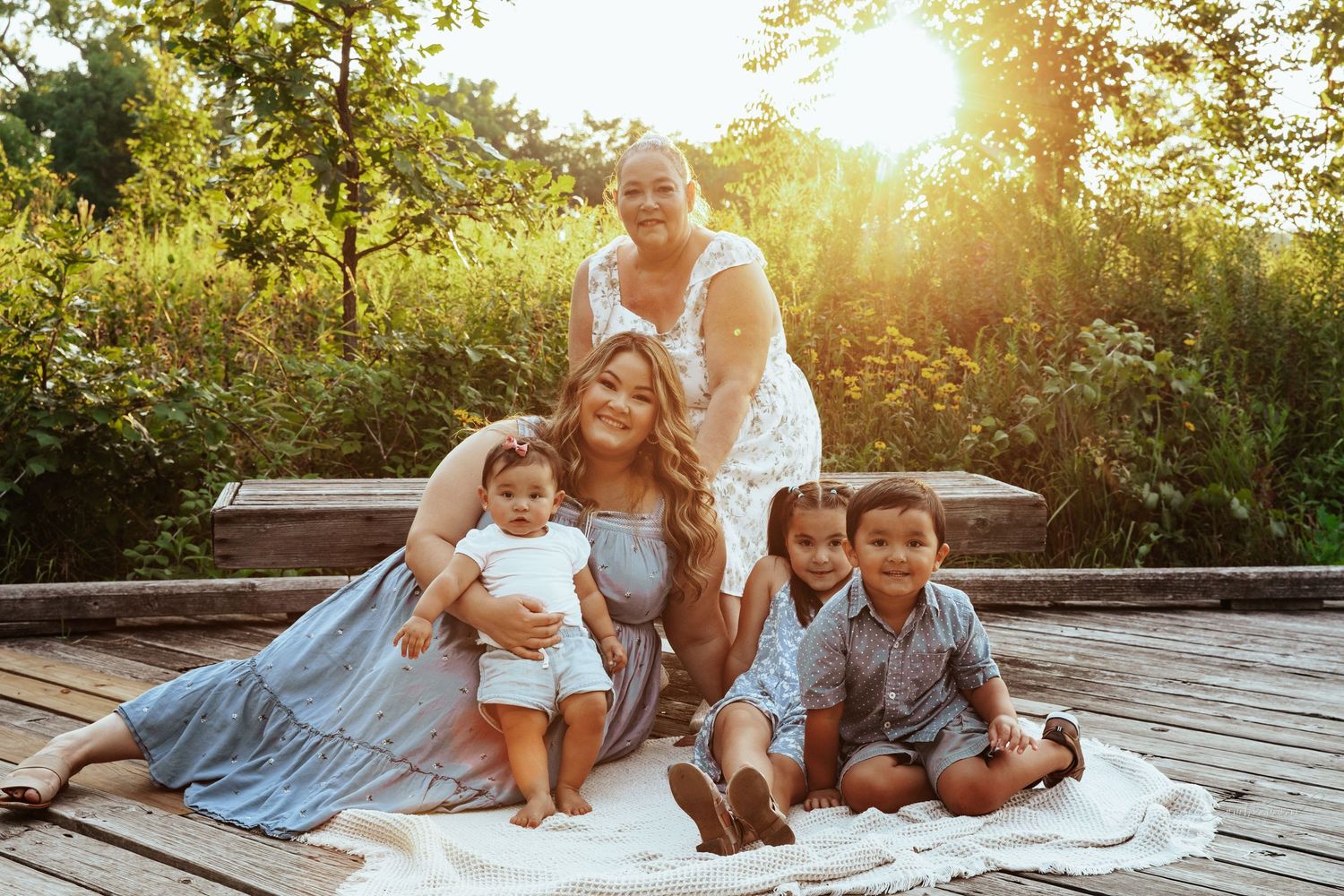 Family sits together on wooden deck during golden hour sunset photoshoot in casual attire.