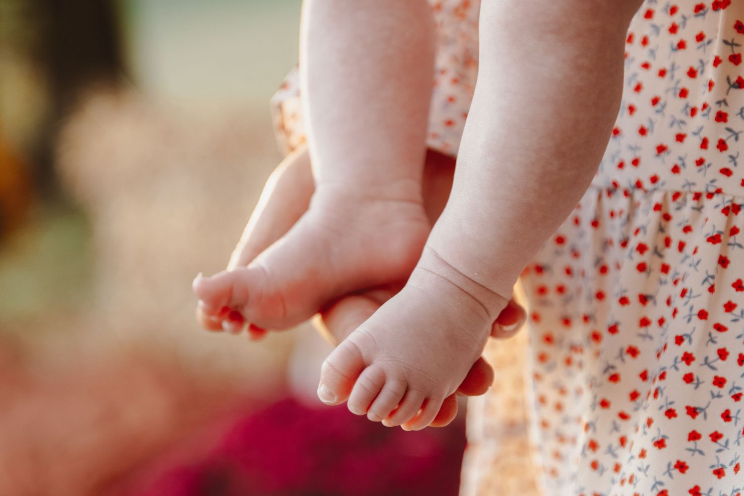 Baby's tiny feet wearing polka dot dress against blurred background in warm lighting.