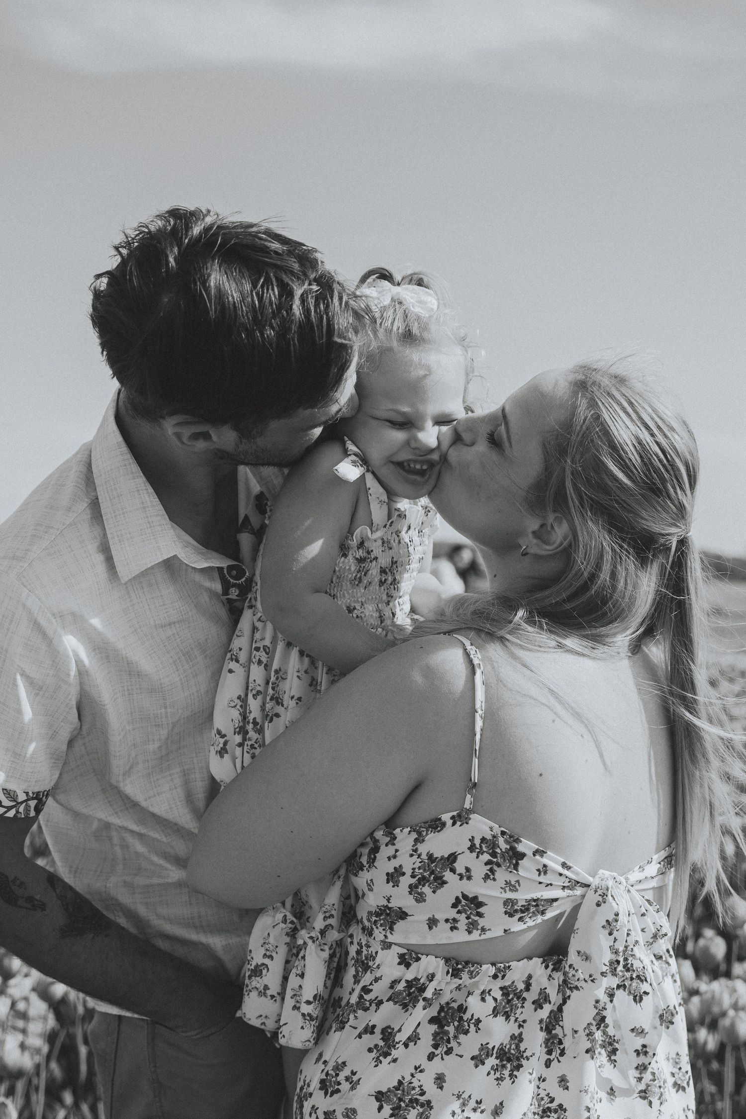 A romantic couple in a field share tender kisses while the woman wears a floral sundress and the man wears a white shirt.