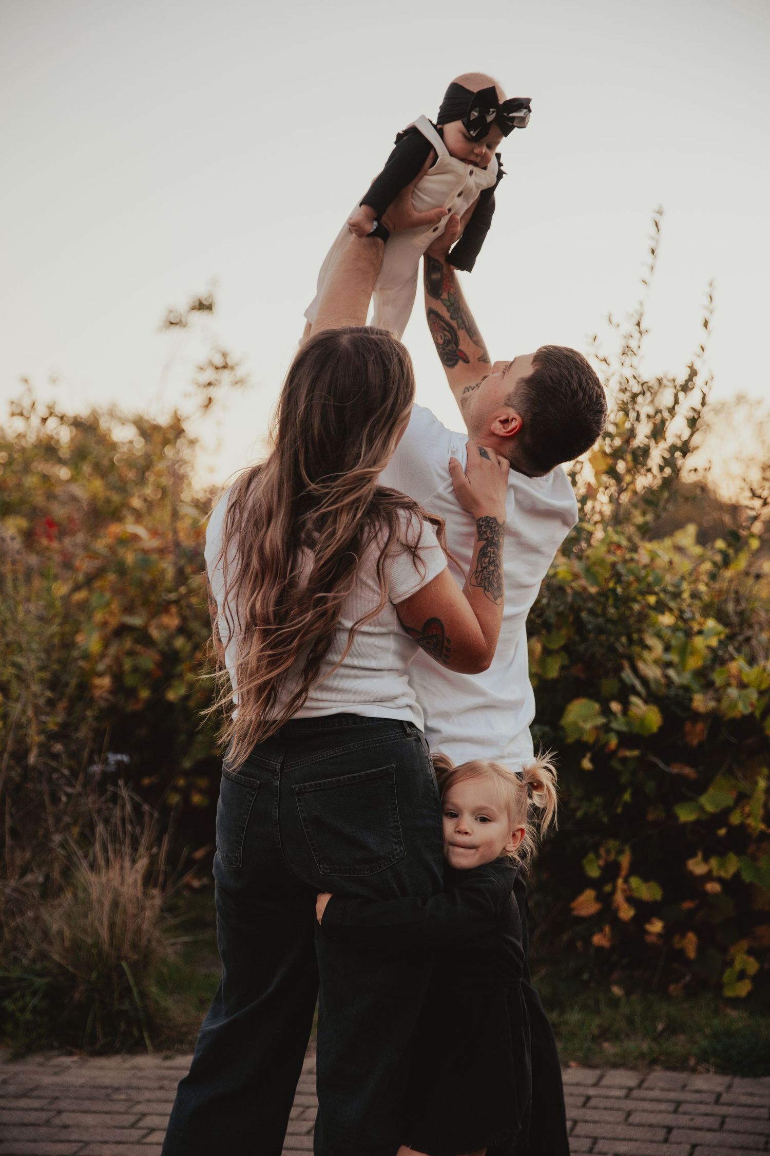 A couple dances together in an outdoor garden setting at sunset while a small child watches nearby.