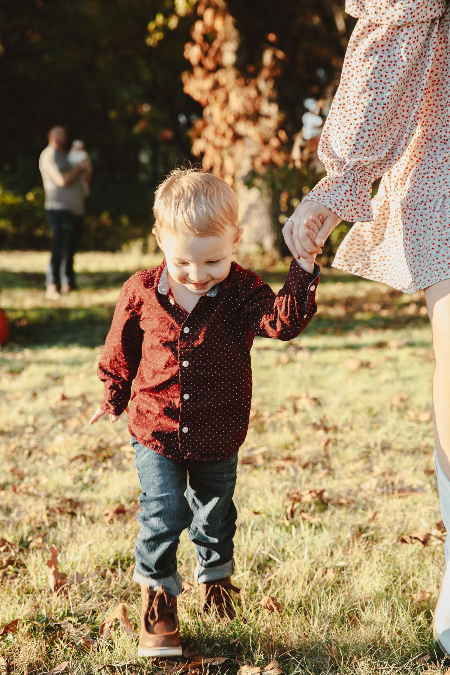 A small child in a polka dot shirt and jeans plays in autumn leaves on a sunny day.