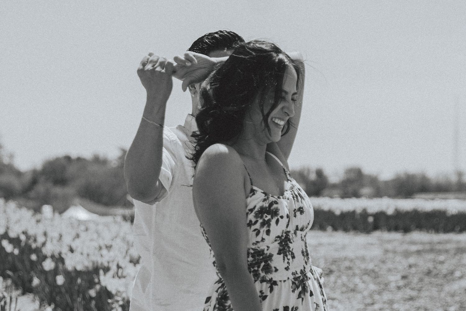 Two people in floral dresses dance together in a black and white photo taken in an outdoor field.