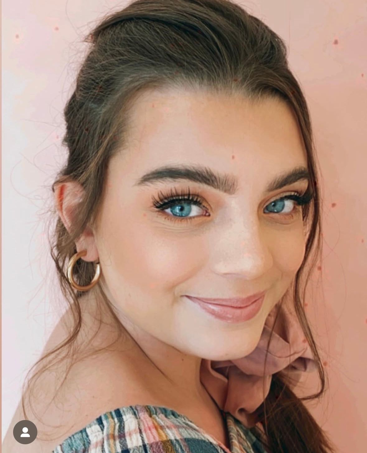 Close-up portrait with striking blue eyes and natural makeup look in soft pink lighting.