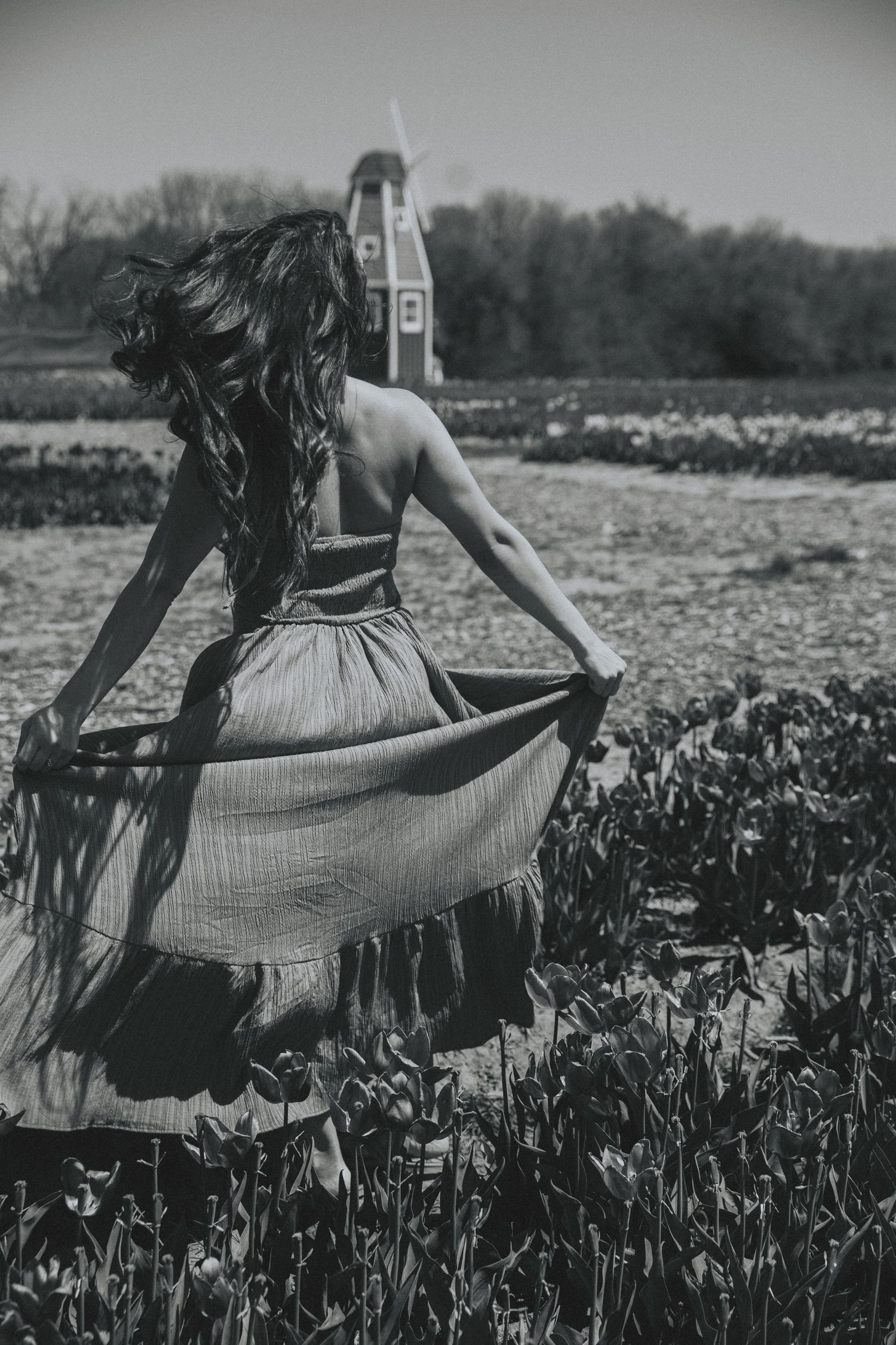 A vintage black and white photo series shows a person in a flowing dress dancing gracefully among blooming flowers in a field.
