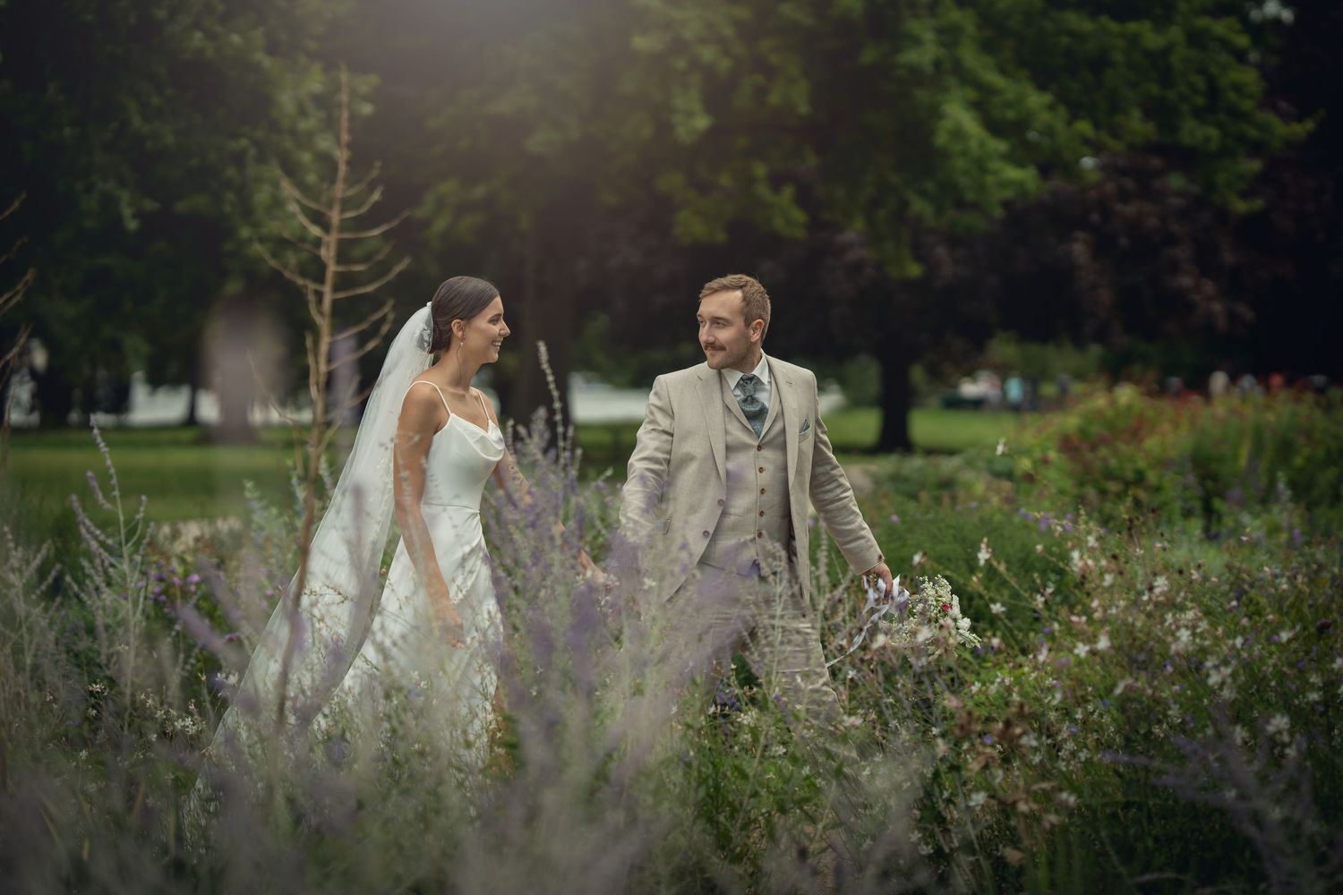Brautpaar läuft fröhlich durch wildes Blumenfeld im Park
