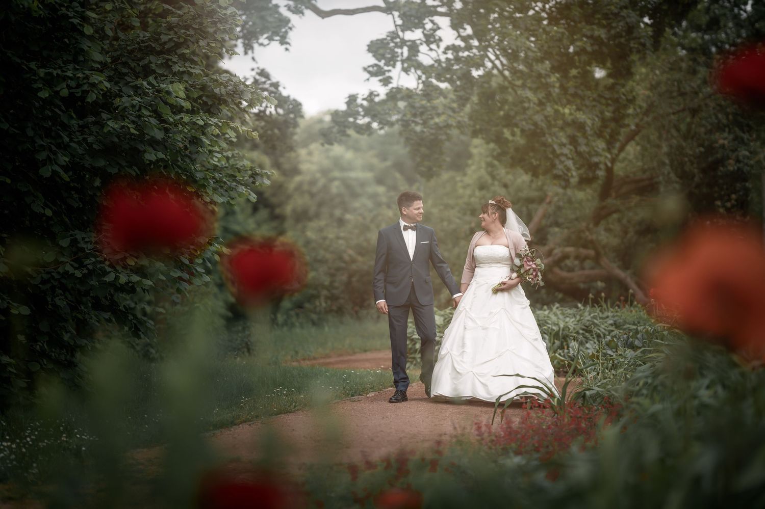 Hochzeitsfotograf Berlin – Brautpaar spaziert durch Naturwiese mit roten Blumen