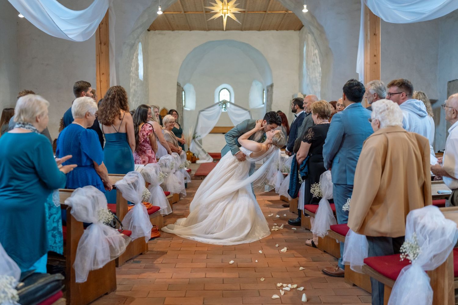 Kirchliche Trauung: Brautpaar küsst sich in der Kirche, Gäste bewerfen sie mit Blumenblättern
