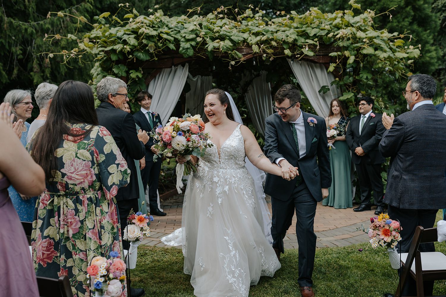 Outdoor wedding ceremony with floral decorations and guests gathered in a garden setting.