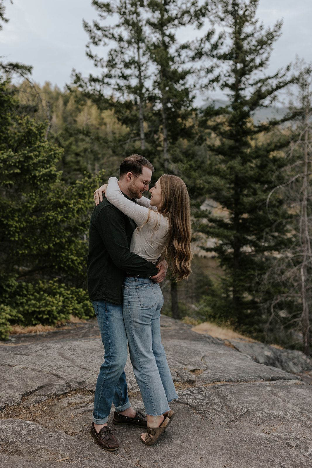 A tender moment shared on a rocky cliff overlooking a forest landscape.