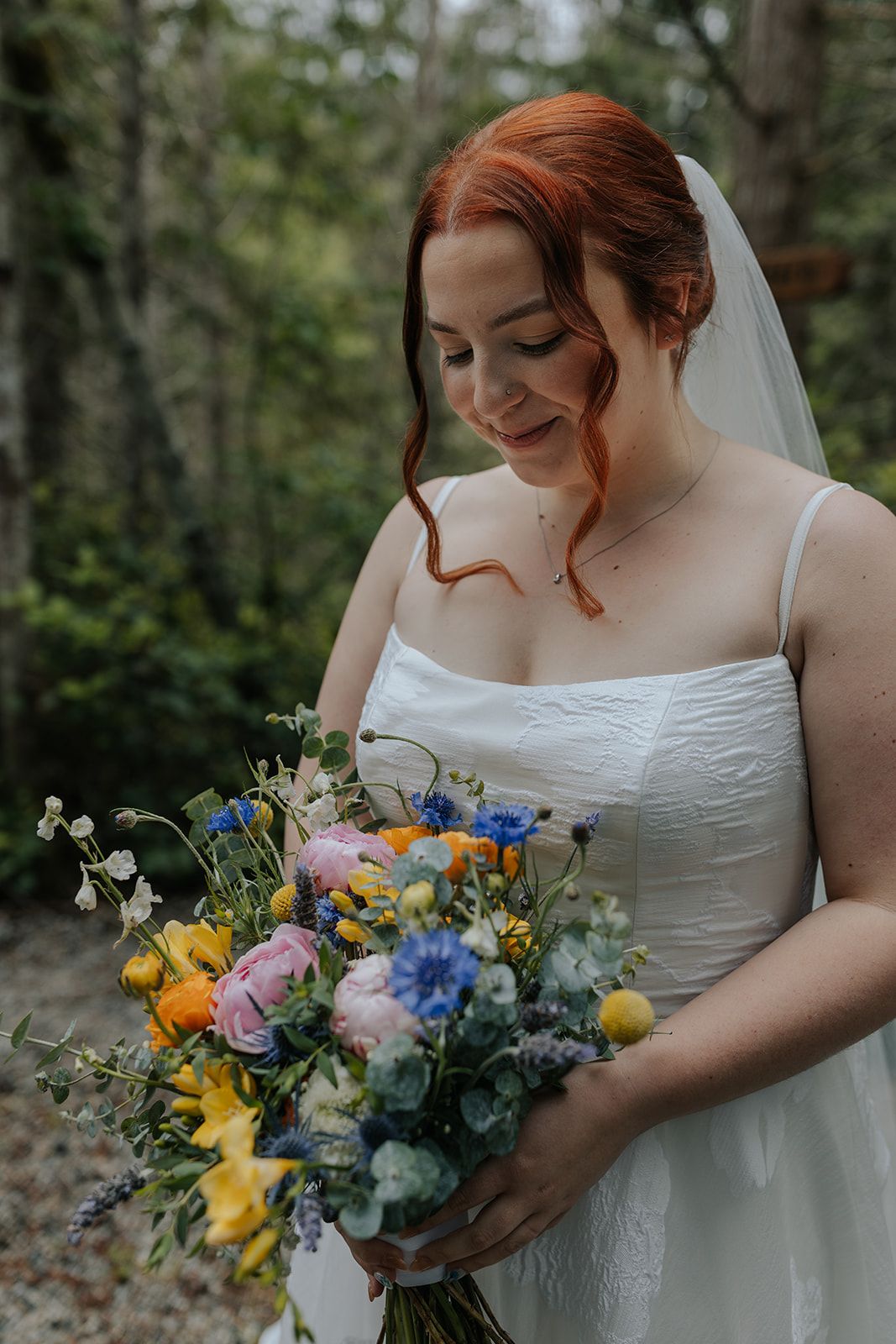 Bridal bouquet with vibrant wildflowers in blue, yellow and pink against a white wedding dress.